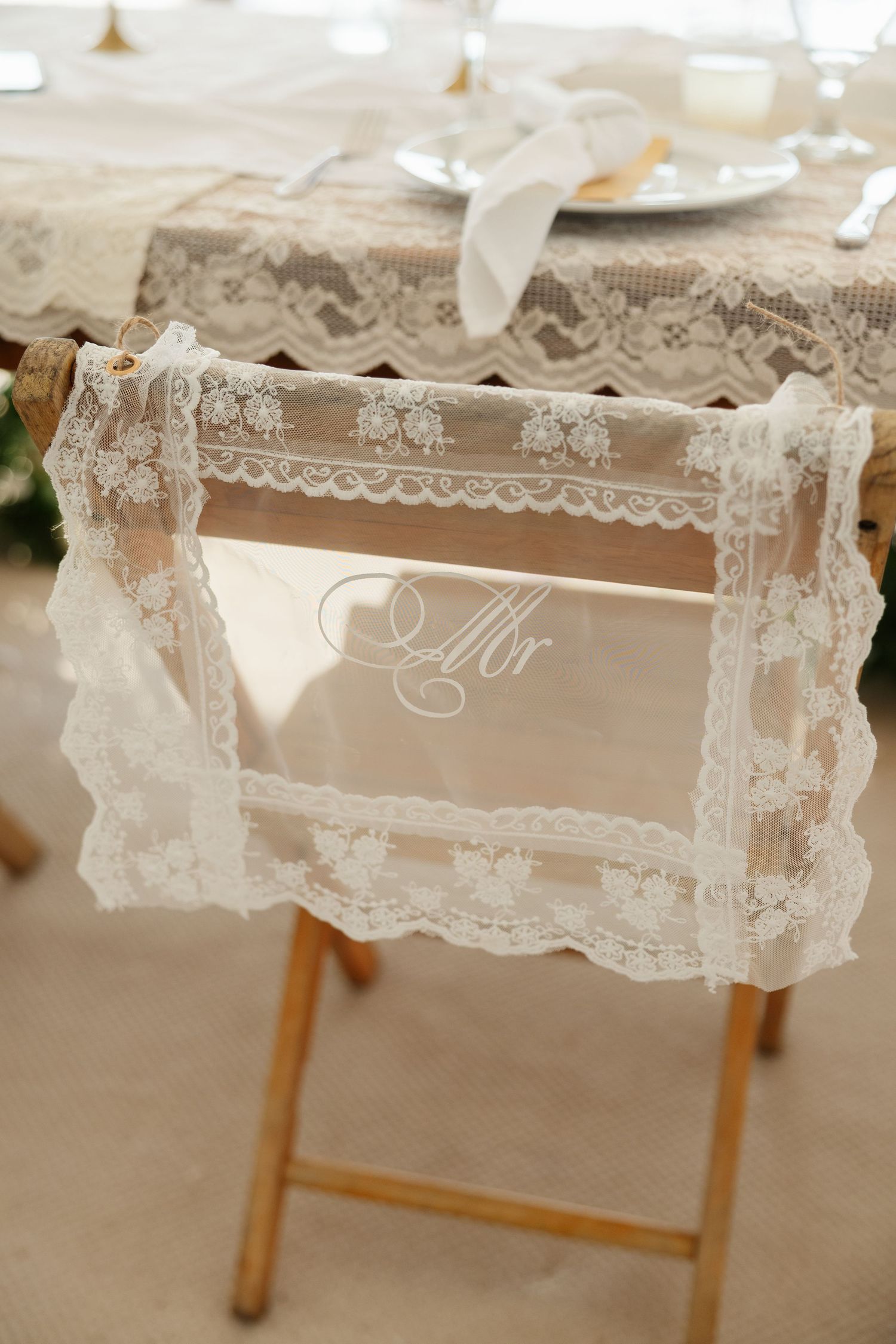 Elegant lace-trimmed chair sign reading Mr decorating a wooden chair at a wedding reception table.