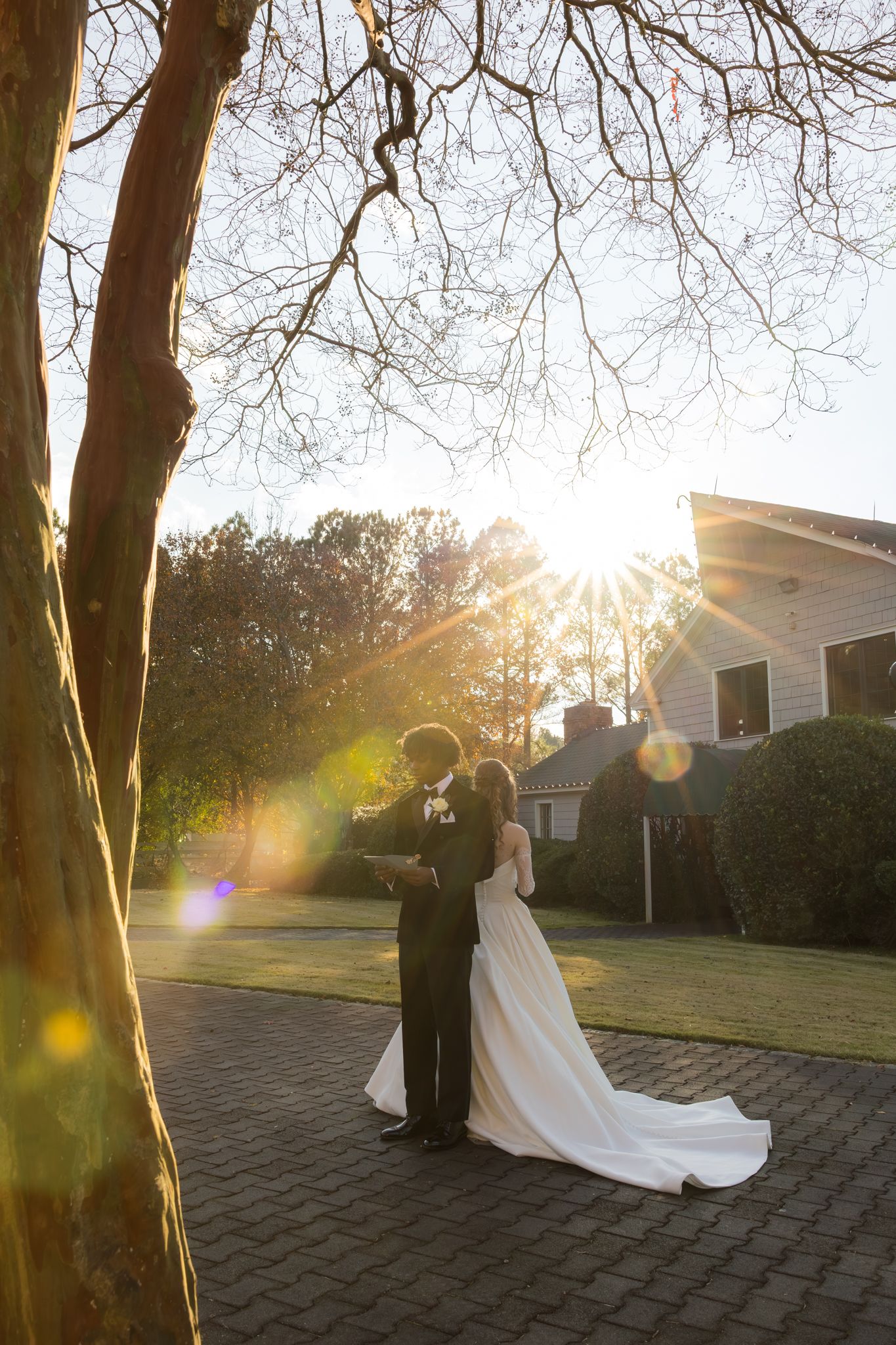 Romantic bride and groom silhouetted against stunning golden sunset on brick pathway at wedding venue.