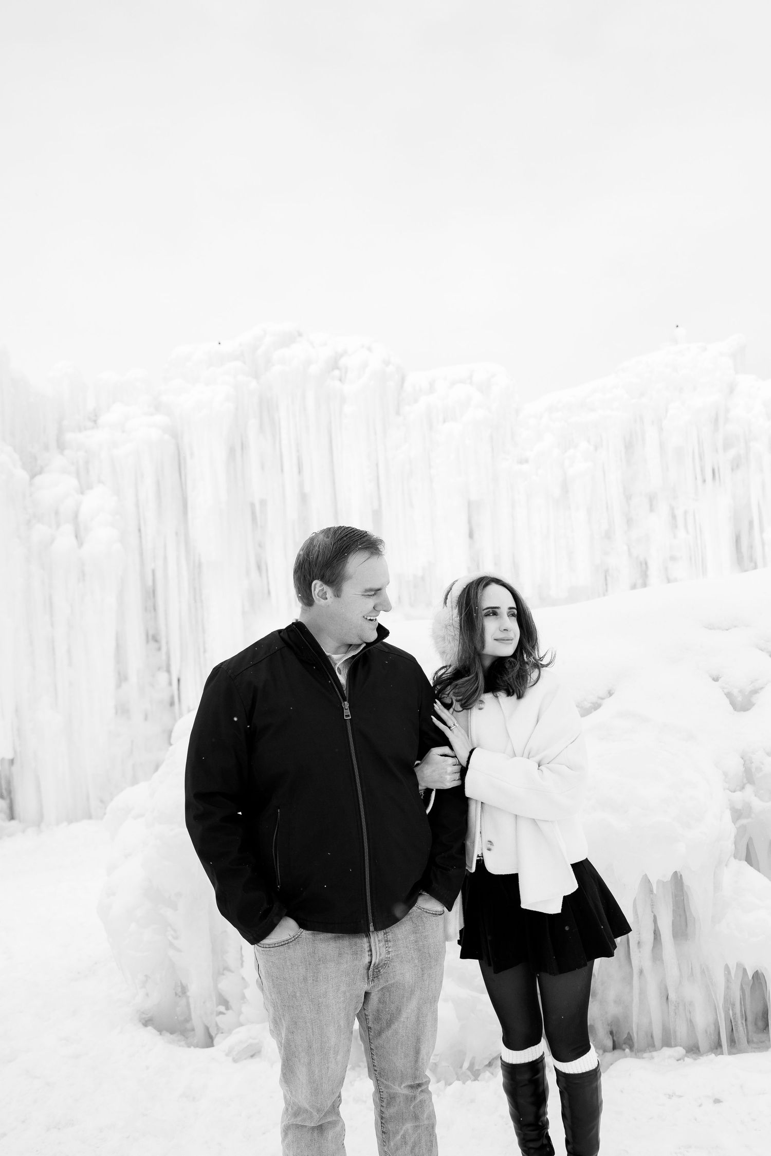 Couple stands together admiring the frozen ice castle formations in a black and white portrait.