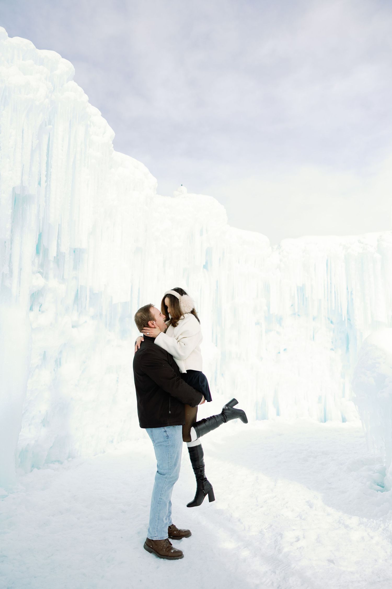 Man lifting his partner joyfully in front of a magnificent ice castle during a winter photo session.
