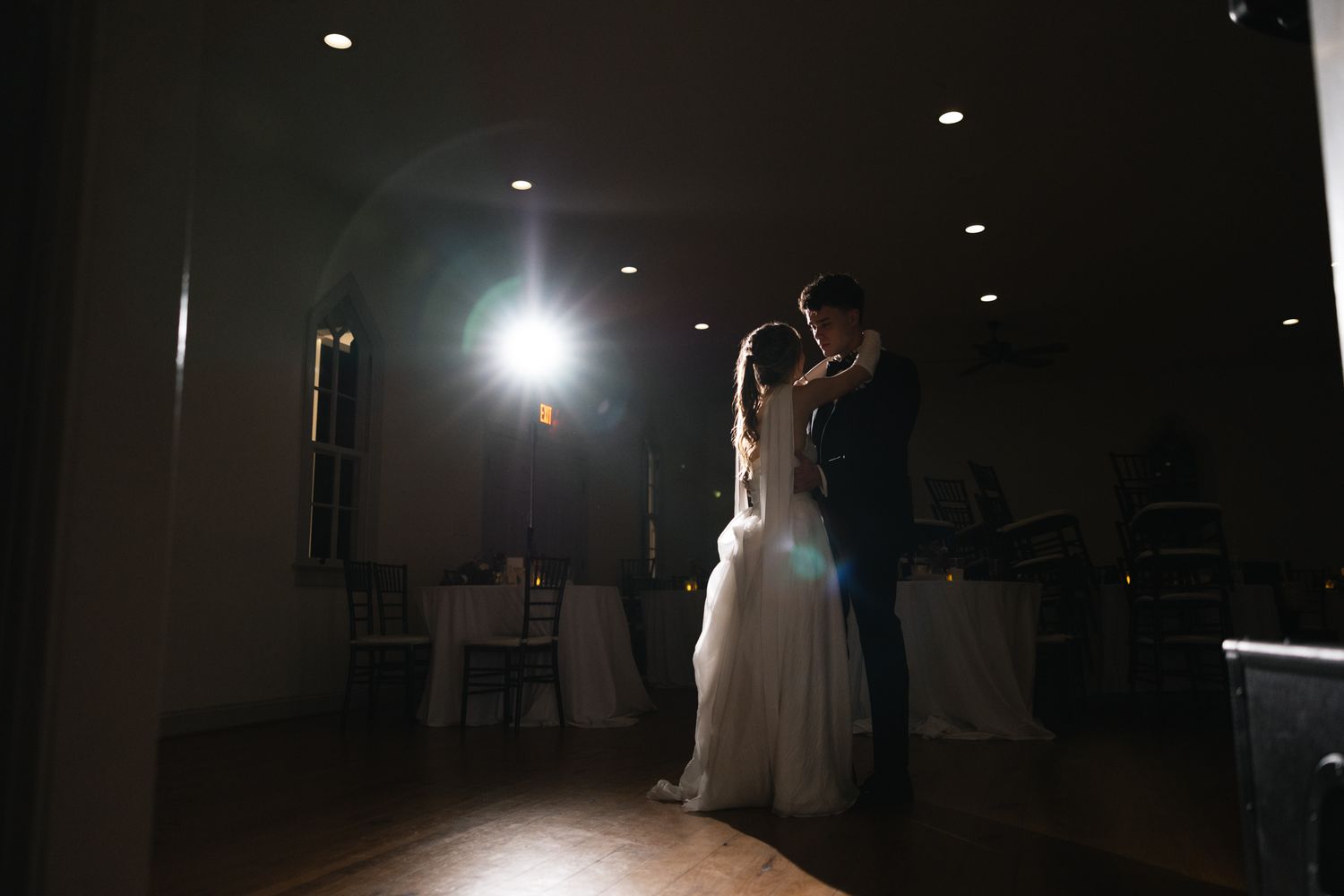 Bride and groom silhouetted during their first dance in a dramatically lit ballroom.