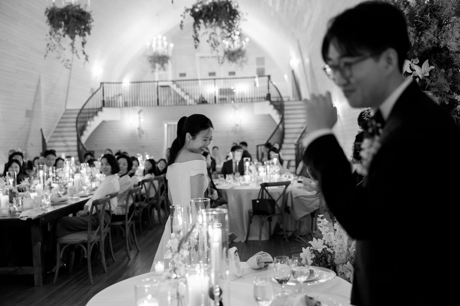 Black and white wedding reception photo with candlelit tables and couple in elegant venue.