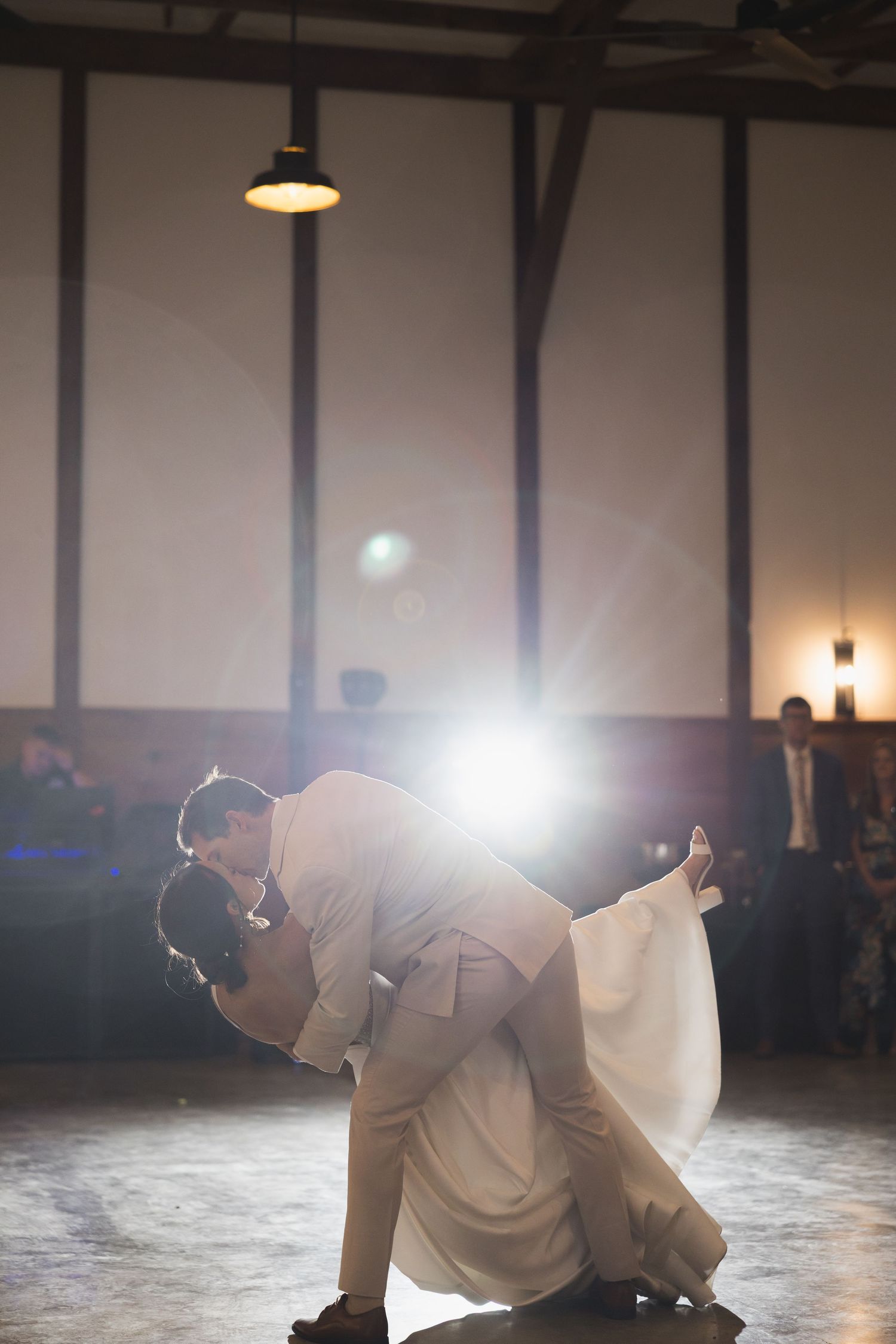Bride and groom share a romantic dip kiss during their first dance at wedding reception.
