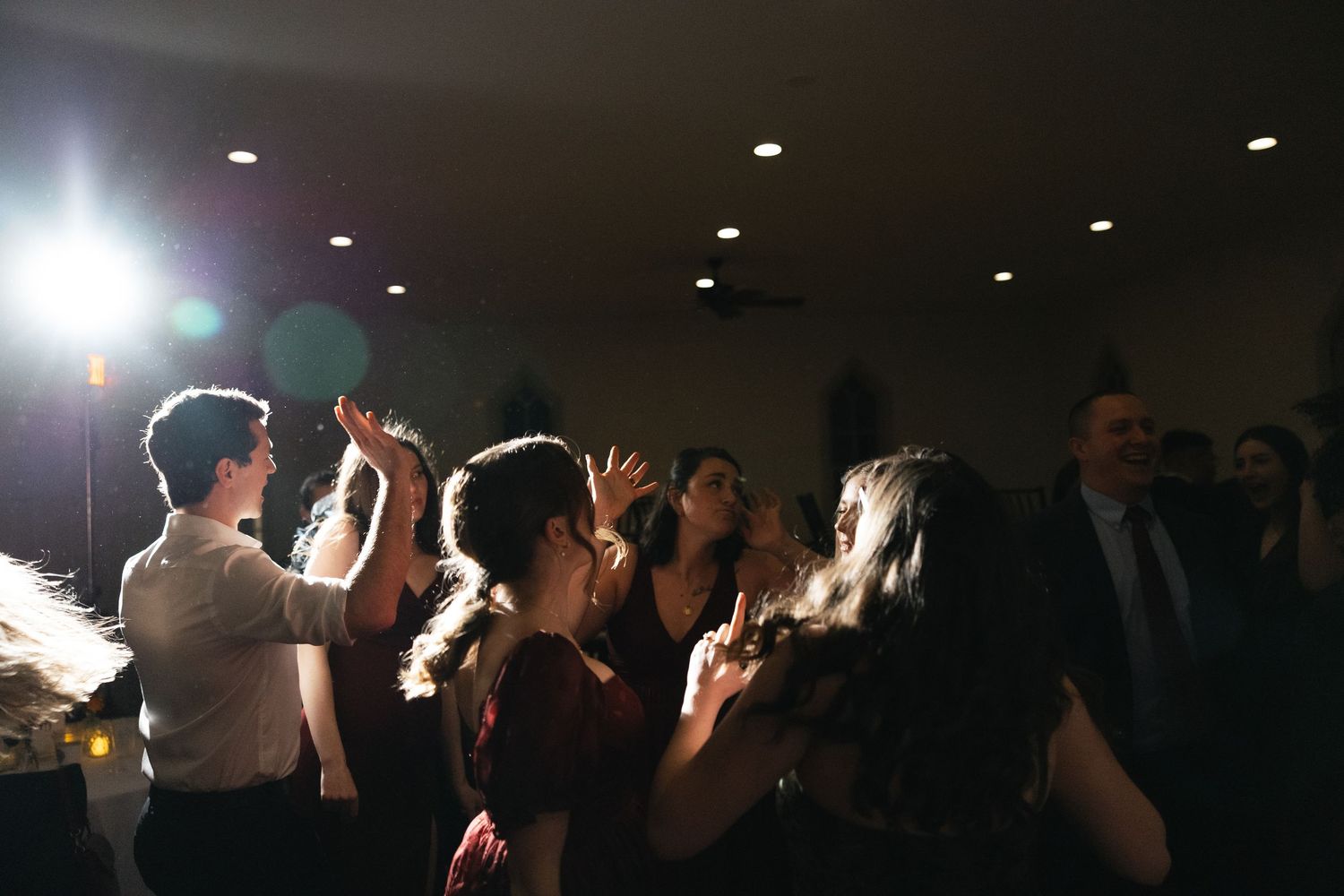 Wedding guests dance and celebrate joyfully on a dimly lit reception dance floor.