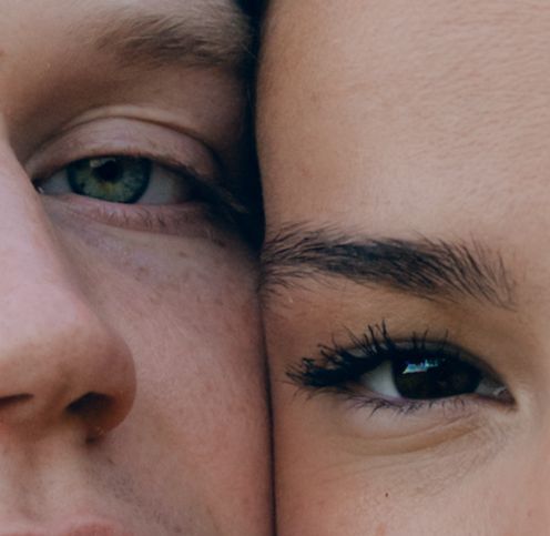 Close-up portrait of two faces side by side showing green and dark eyes in intimate detail.