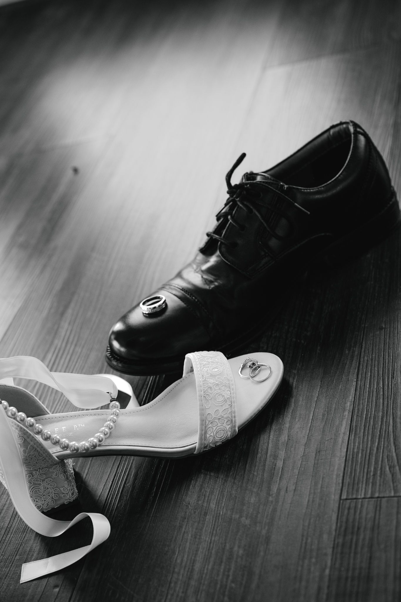 Black and white photo of bride and groom wedding shoes on hardwood floor.