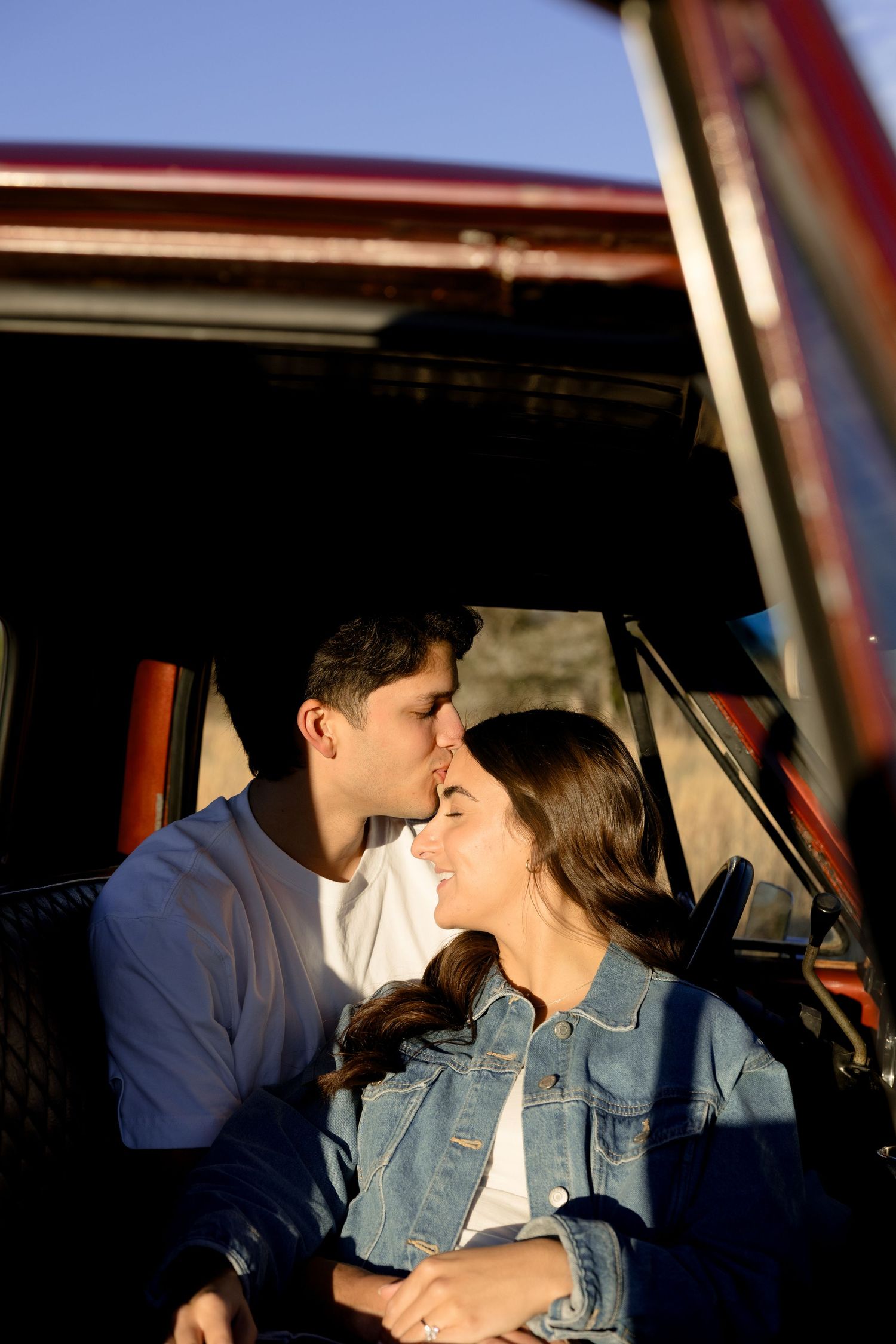 Couple sharing a tender moment near the open door of a classic red truck at sunset.