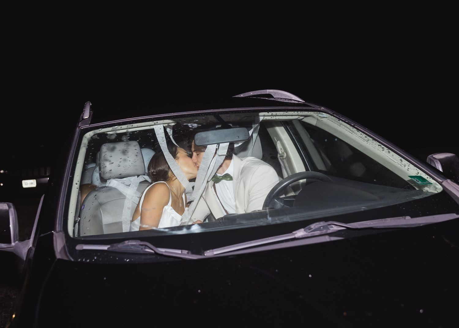 Bride and groom sitting in car at night after wedding reception departure.