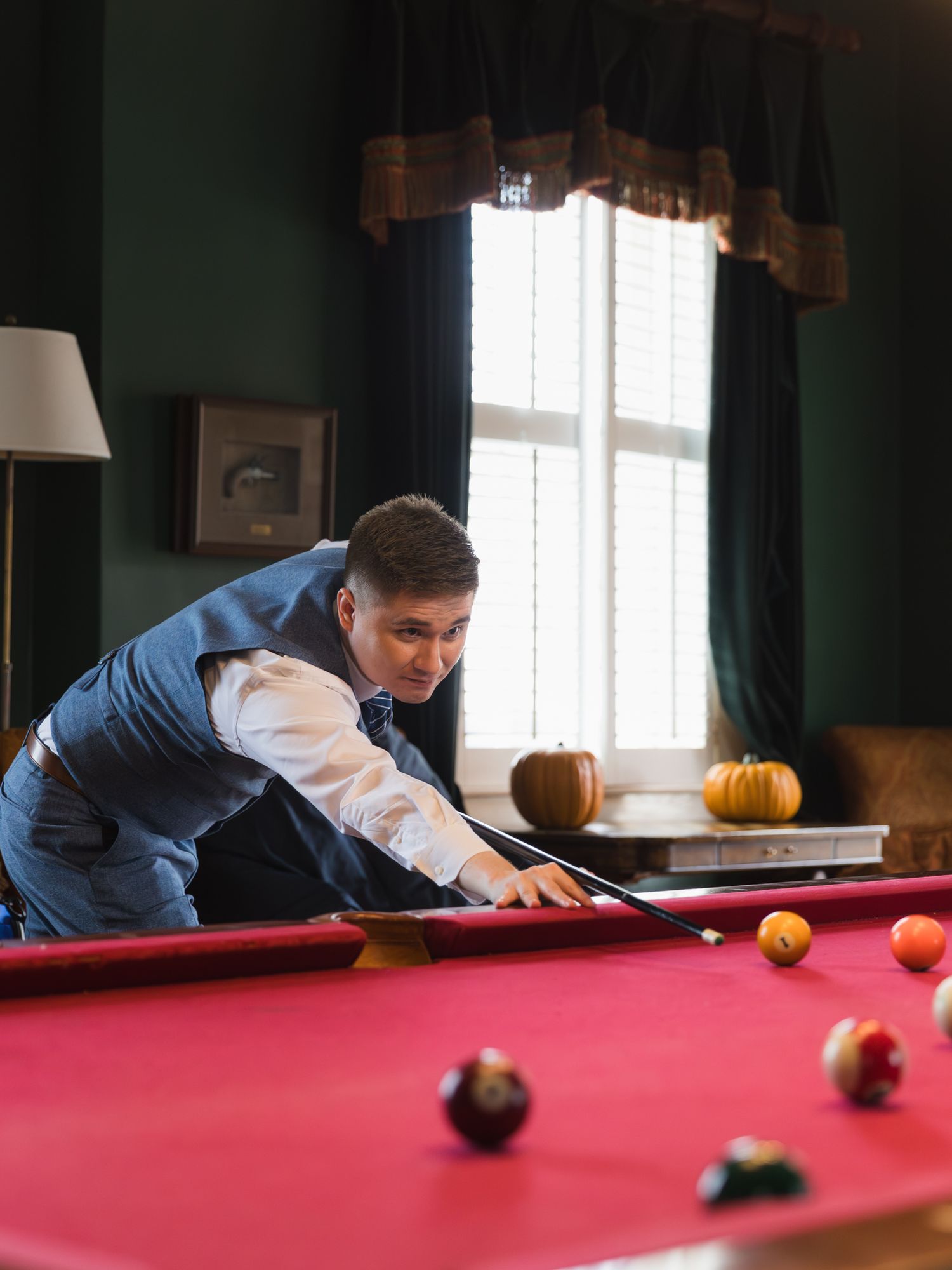 Man in blue vest leaning over a red billiard table taking a pool shot in an elegant game room.