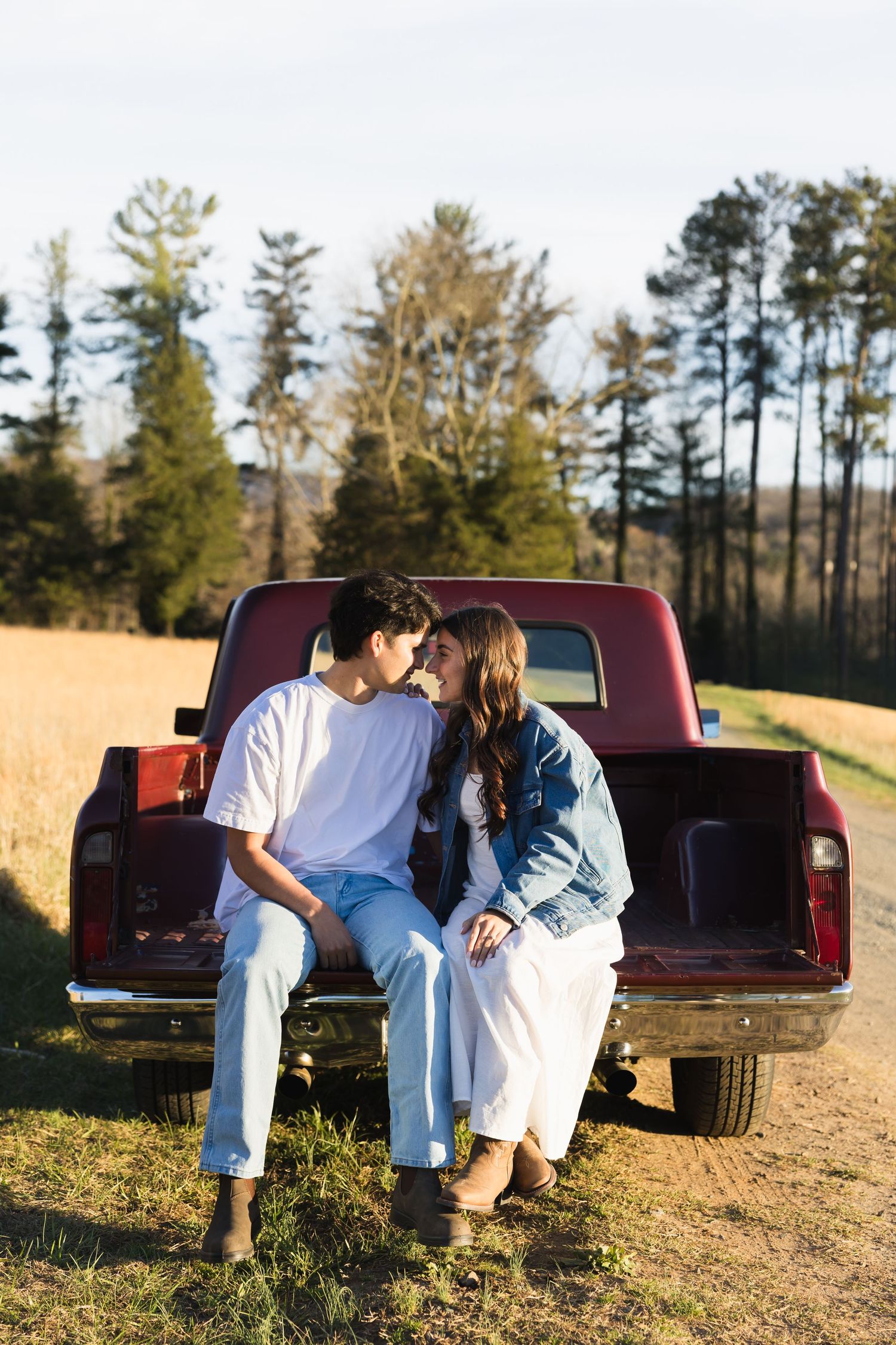Couple sitting on the tailgate of a red vintage truck, sharing a romantic moment outdoors.