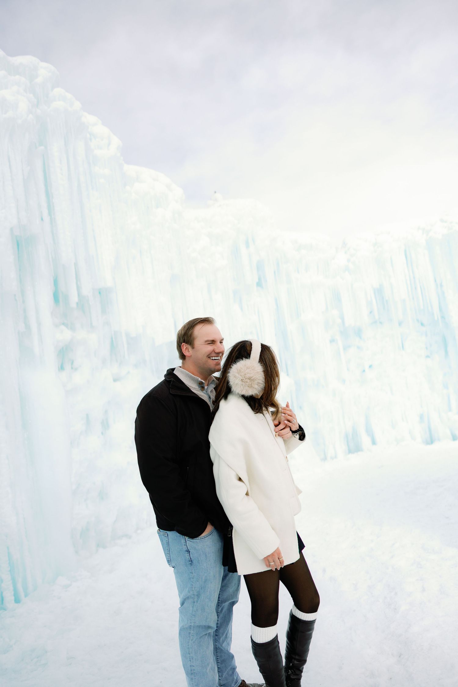 Happy couple holding hands and smiling together beside stunning blue ice castle formations in winter.