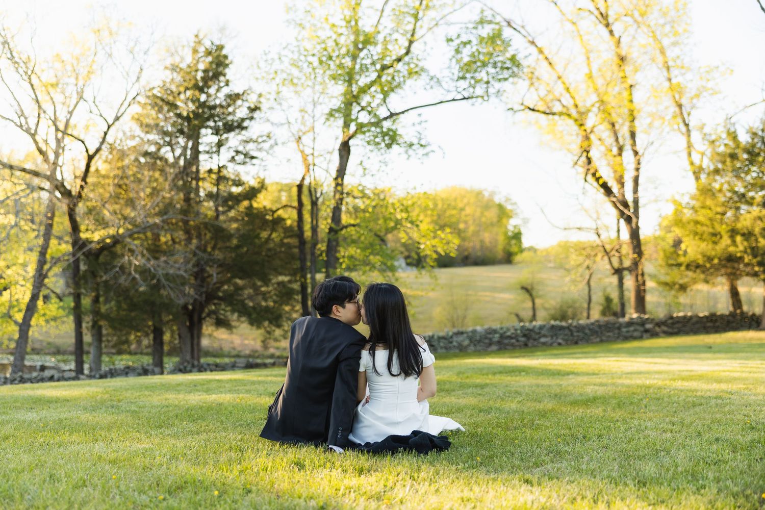 Couple in wedding attire sitting together on grass, sharing a quiet moment in a sunny park.