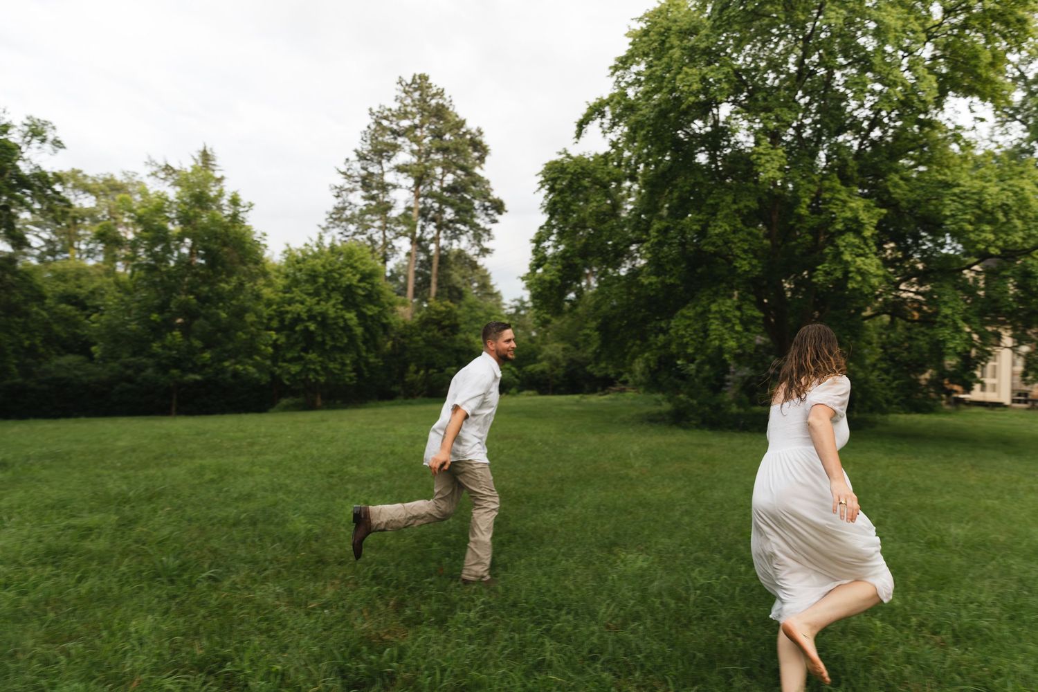 Joyful couple running through a lush green park lawn on a cloudy day.