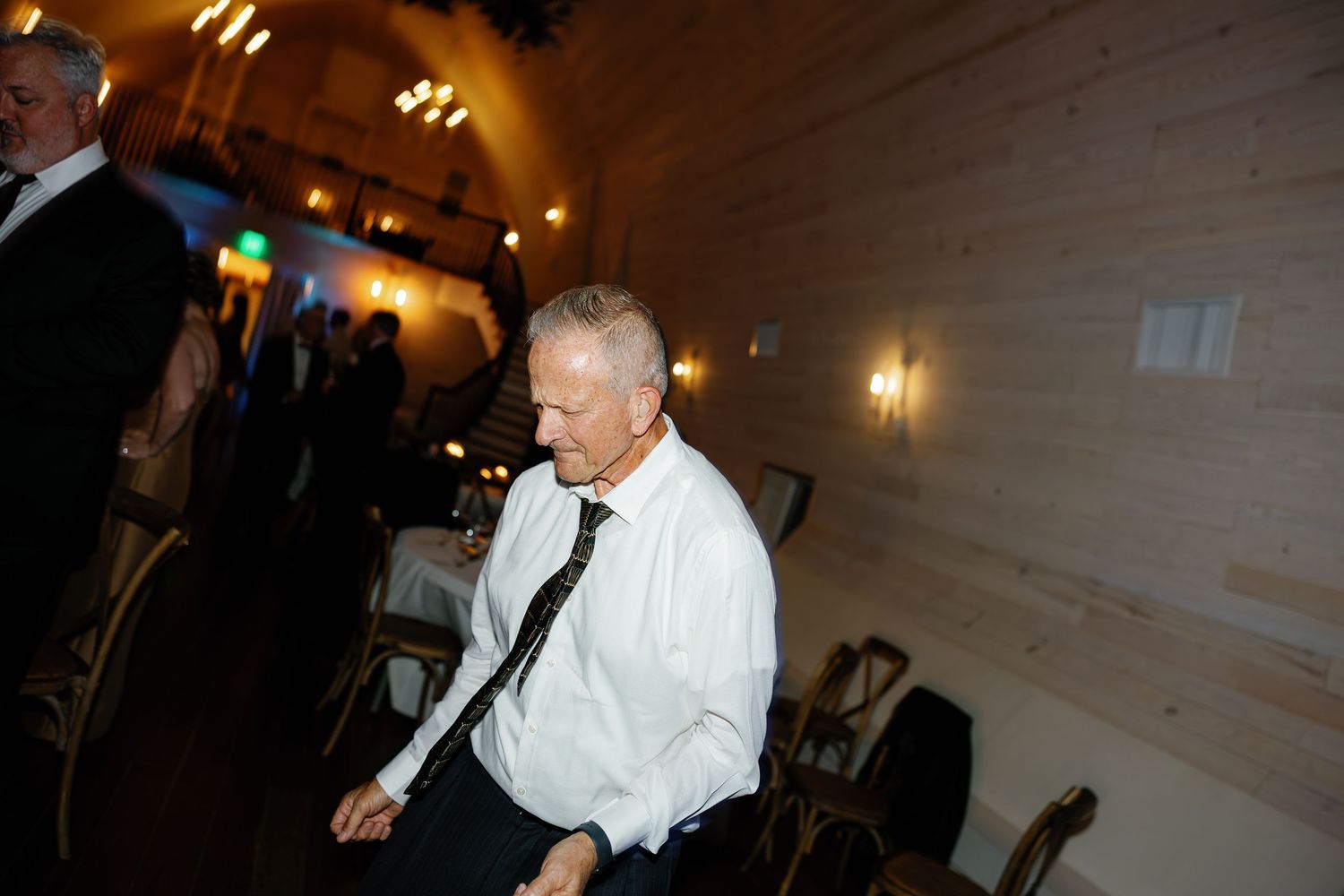Elderly wedding guest in white shirt and tie dances alone at wedding reception venue.