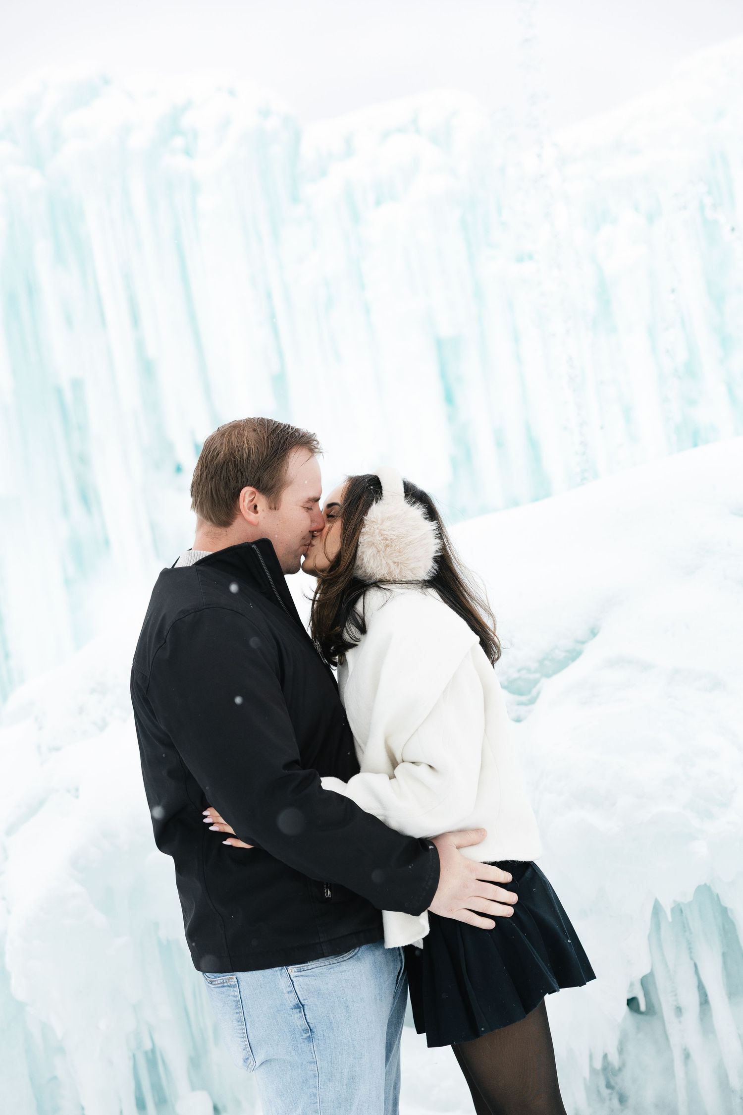 Couple shares a romantic kiss in front of towering blue ice formations at an ice castle.