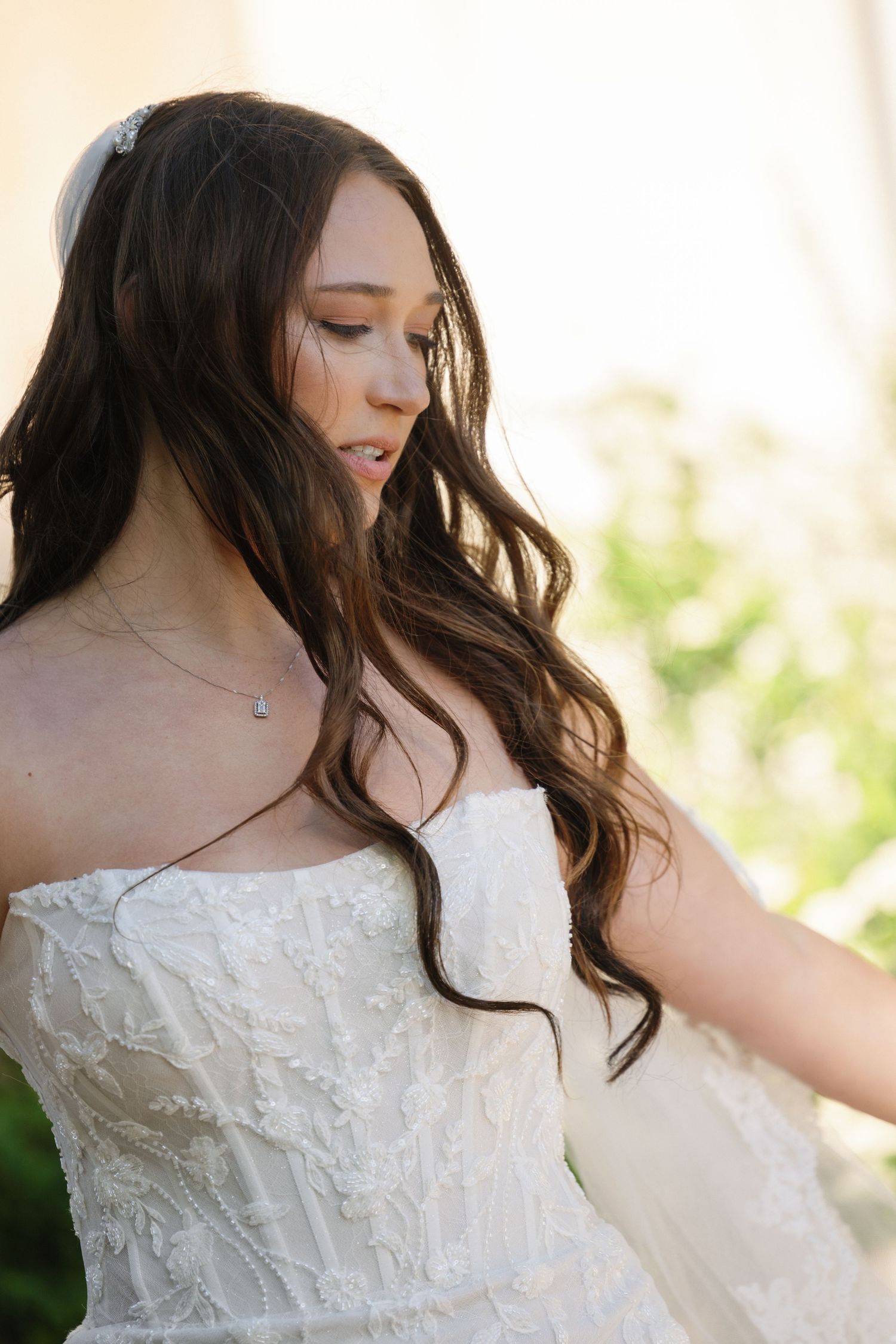 Close-up of a bride with long wavy hair in a strapless lace wedding gown with a delicate hair accessory.
