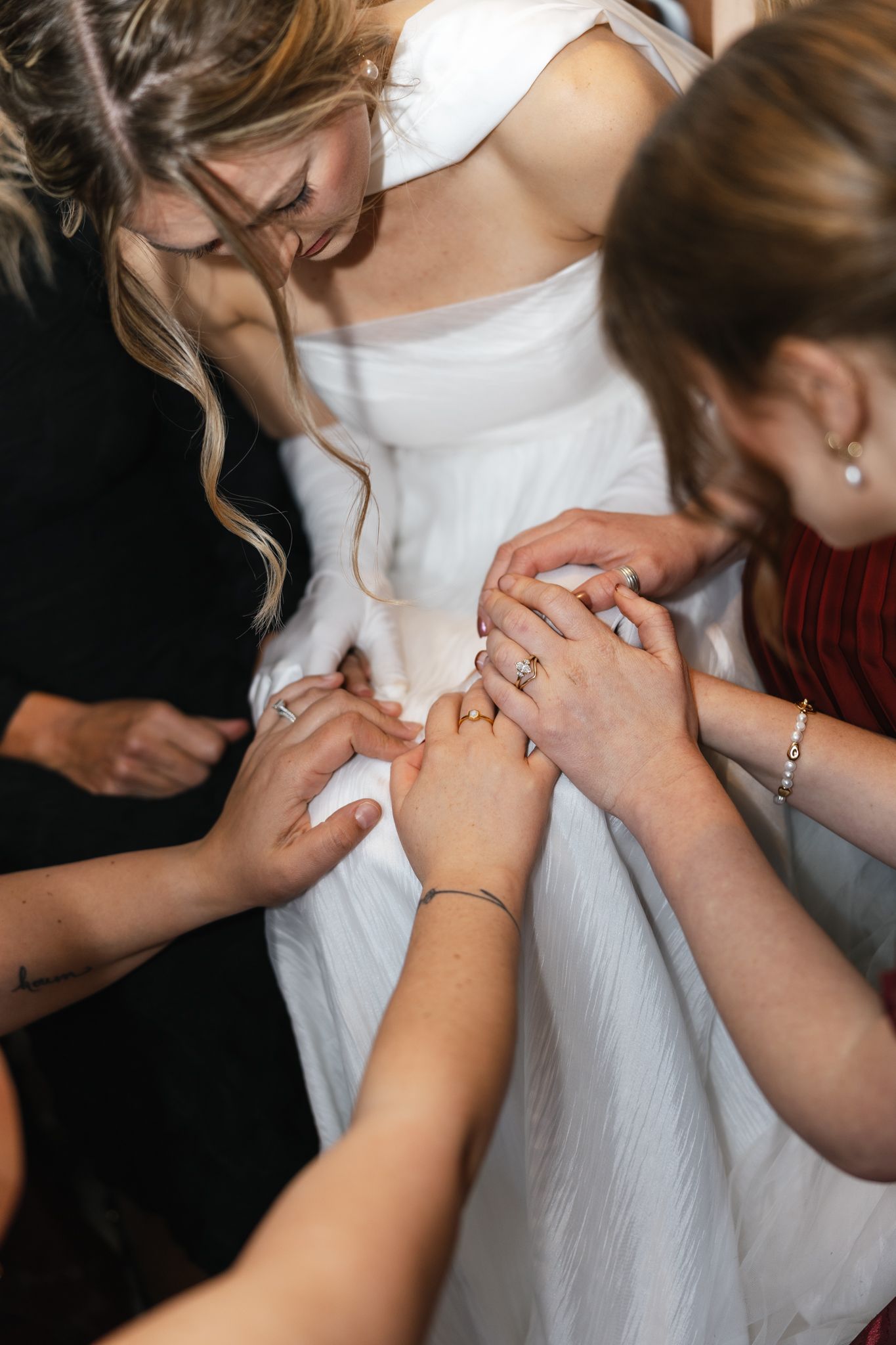Bridesmaids and bride join hands together in a circle during emotional pre-wedding prayer ceremony.