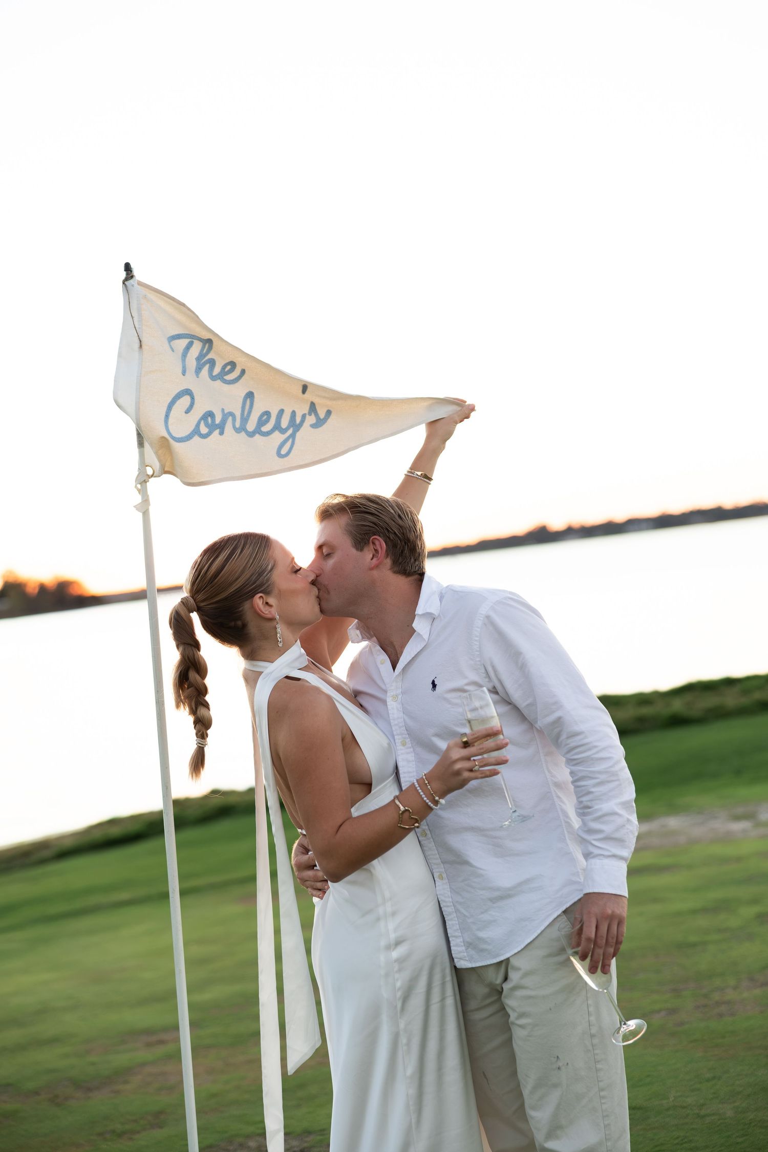 Couple kissing beside a decorative pennant flag reading The Conkleys at an outdoor waterfront wedding celebration.