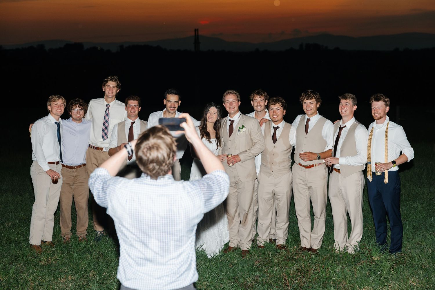 Group of young adults in formal attire posing for a photo at sunset outdoors.