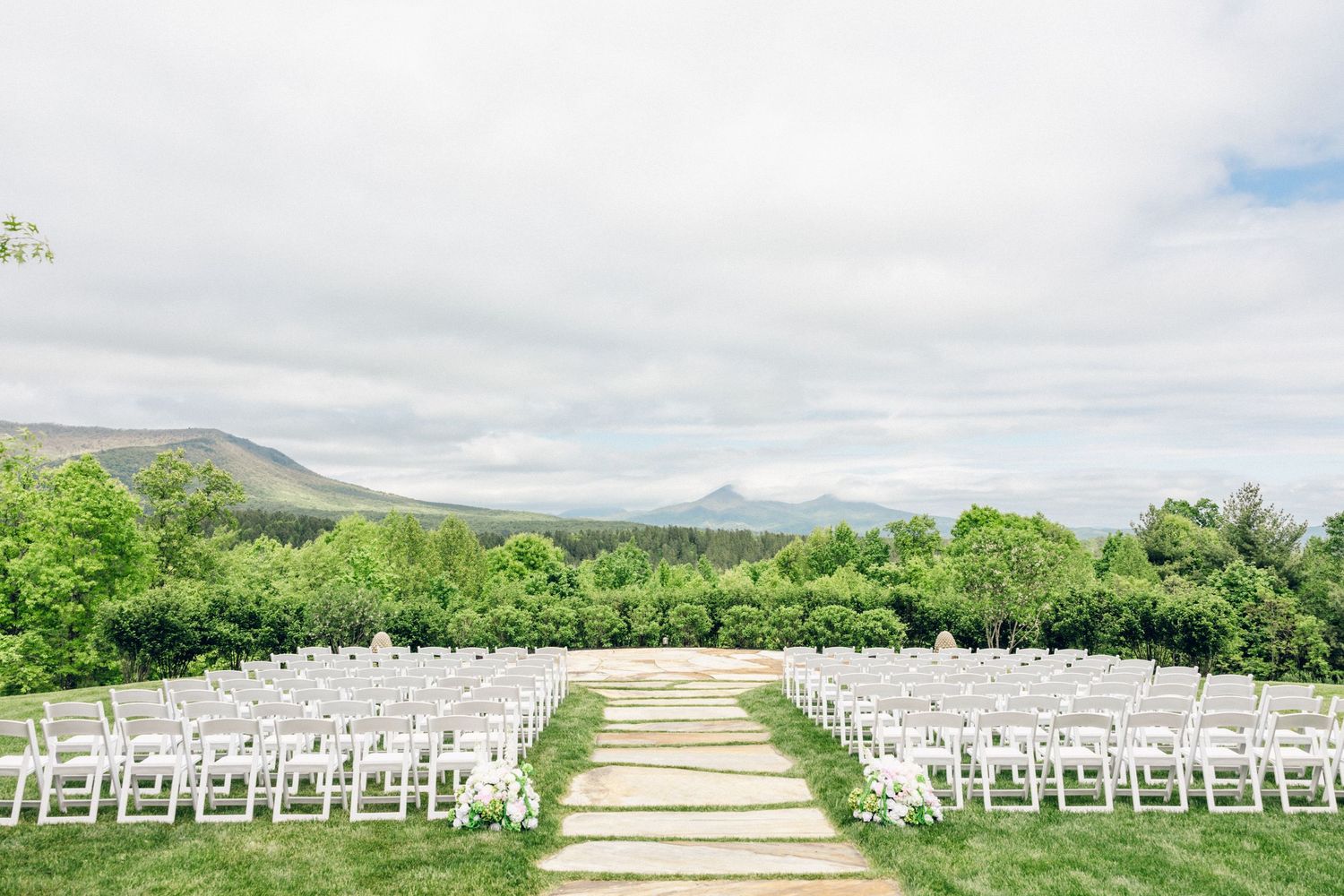 Outdoor wedding ceremony setup with white chairs and mountain views.