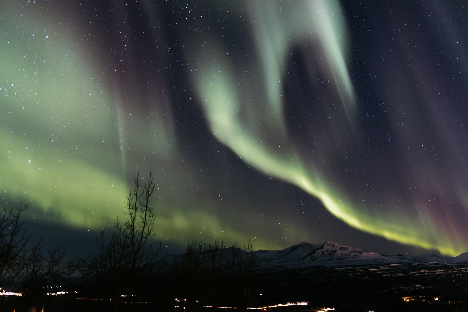 Spectacular aurora borealis northern lights display with vivid green and purple waves over dark mountain landscape.