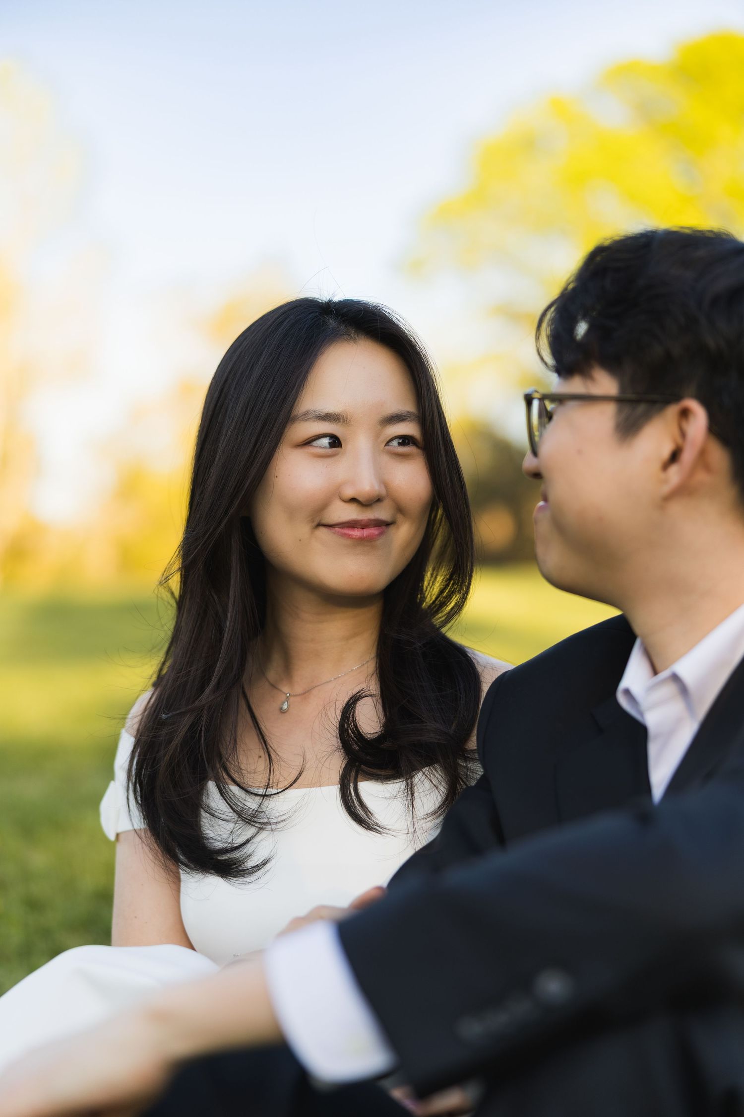 Close-up of a smiling bride looking at her groom while sitting outdoors in golden evening light.