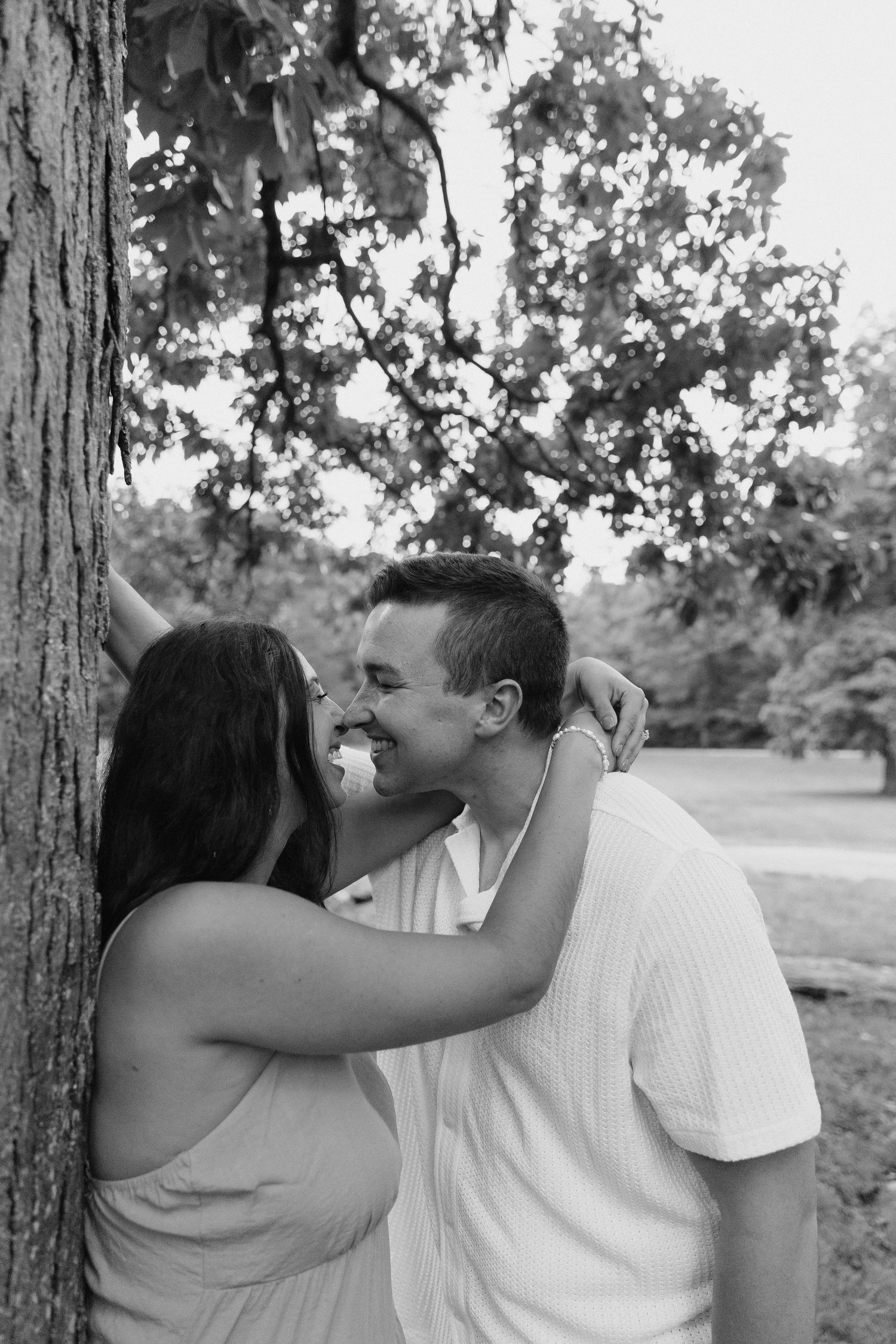 Black and white photo of couple laughing together by a tree.