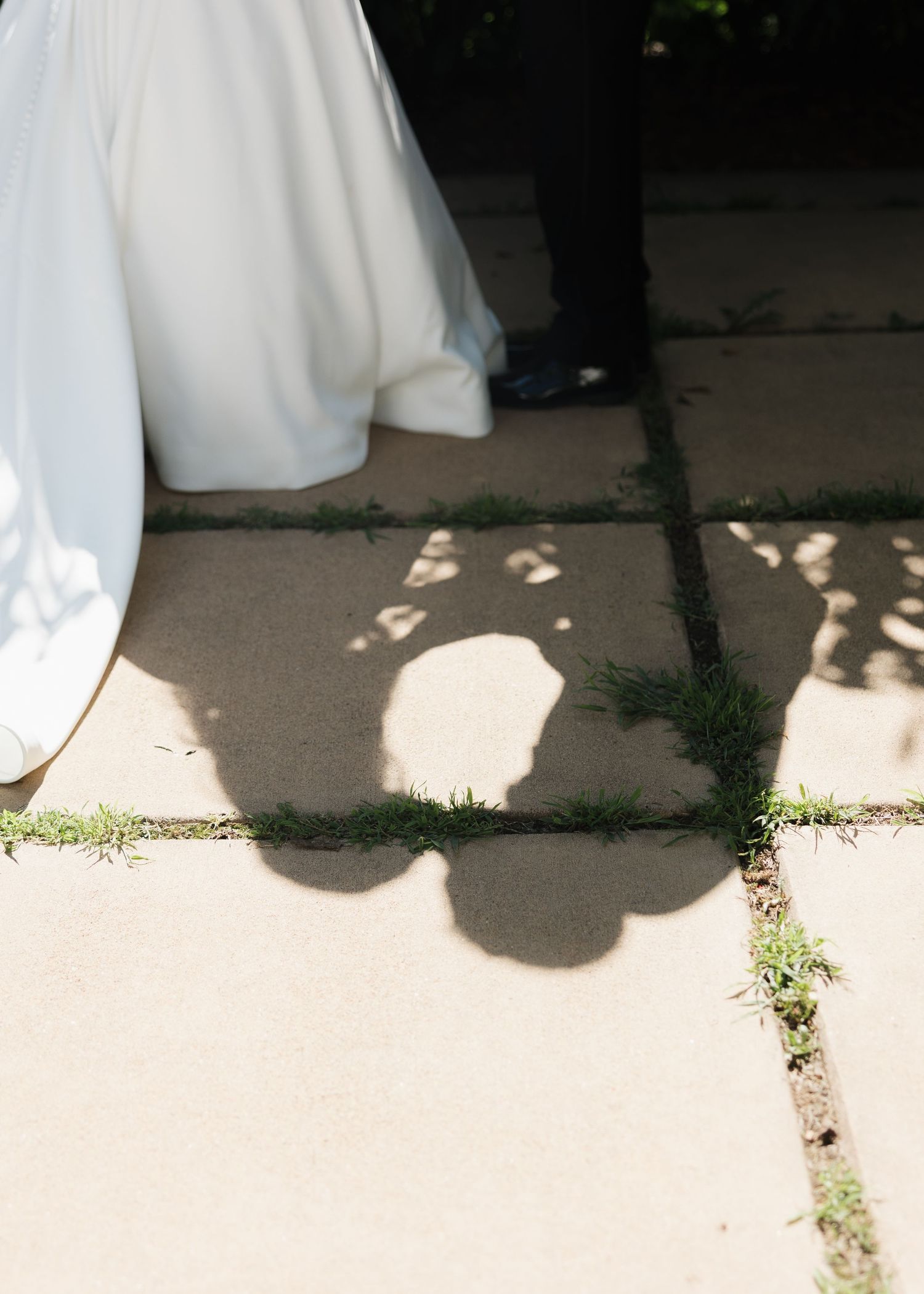 Shadows of a bride in white gown and groom in dark suit cast on sunlit stone pavement at a wedding.