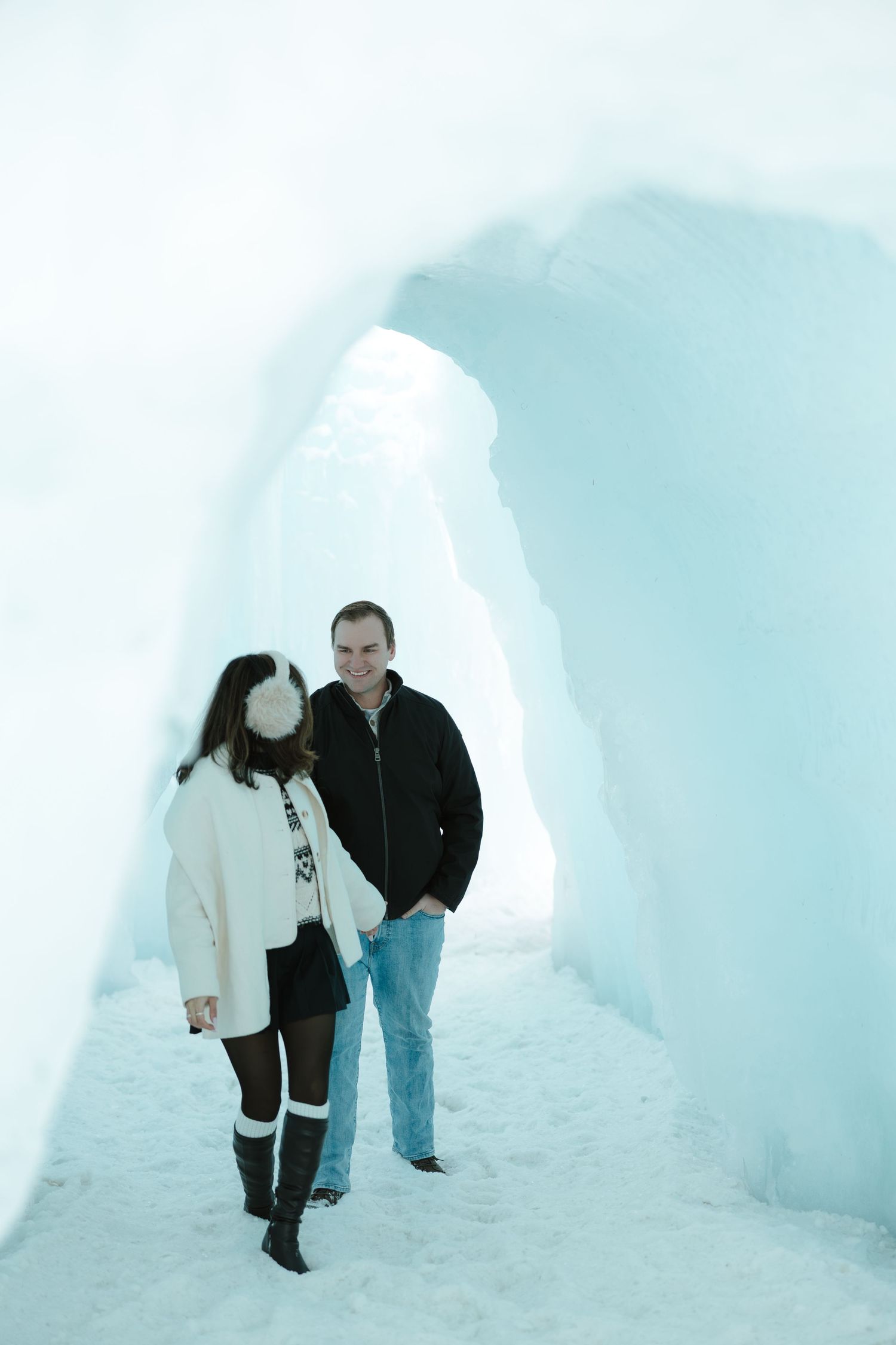 Happy couple walking through a magical ice castle tunnel during a romantic winter engagement shoot.