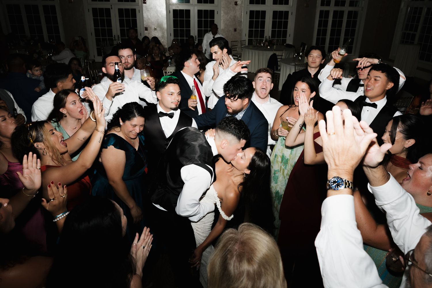 Guests in formal attire dance together at a lively wedding reception celebration.