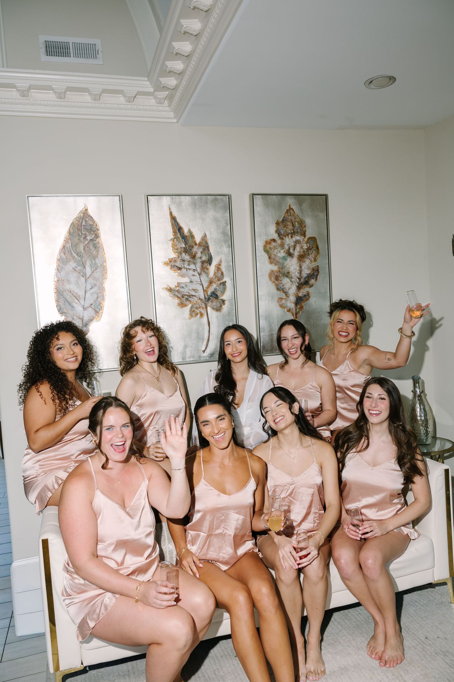 Group of bridesmaids in matching blush satin pajamas celebrating together in a beautifully decorated room.