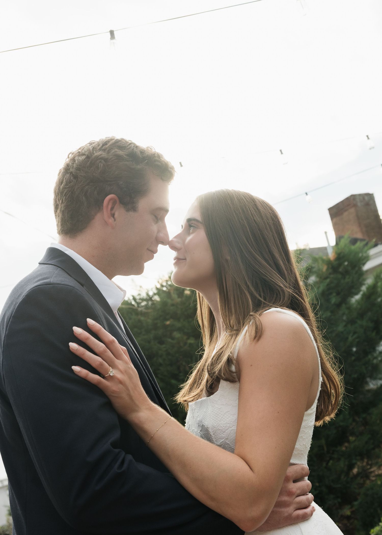A couple in wedding attire share a romantic moment outdoors, gazing into each other's eyes with soft natural lighting.