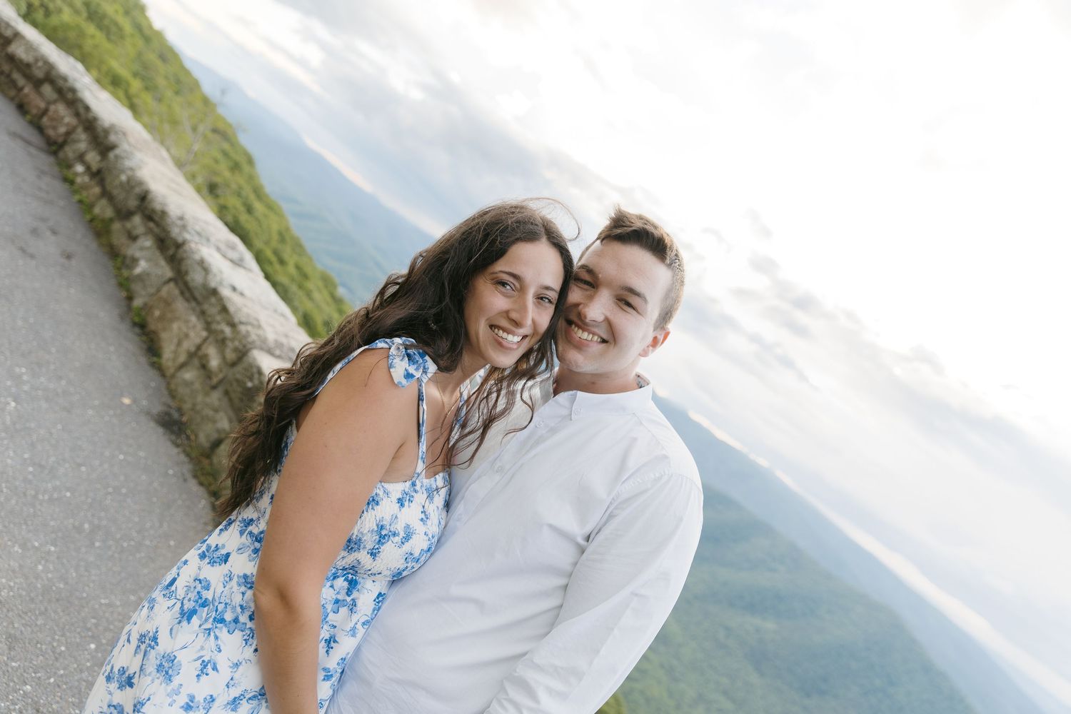 Happy couple smiling together at a scenic mountain overlook during their engagement photo session.