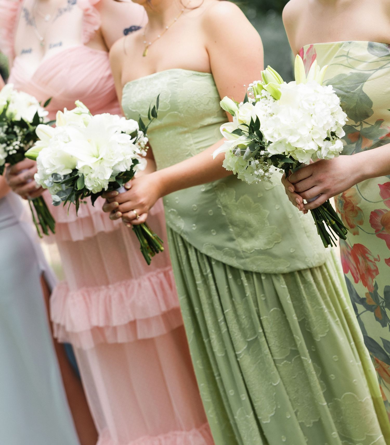 Bridesmaids in mismatched pastel dresses holding white floral bouquets.
