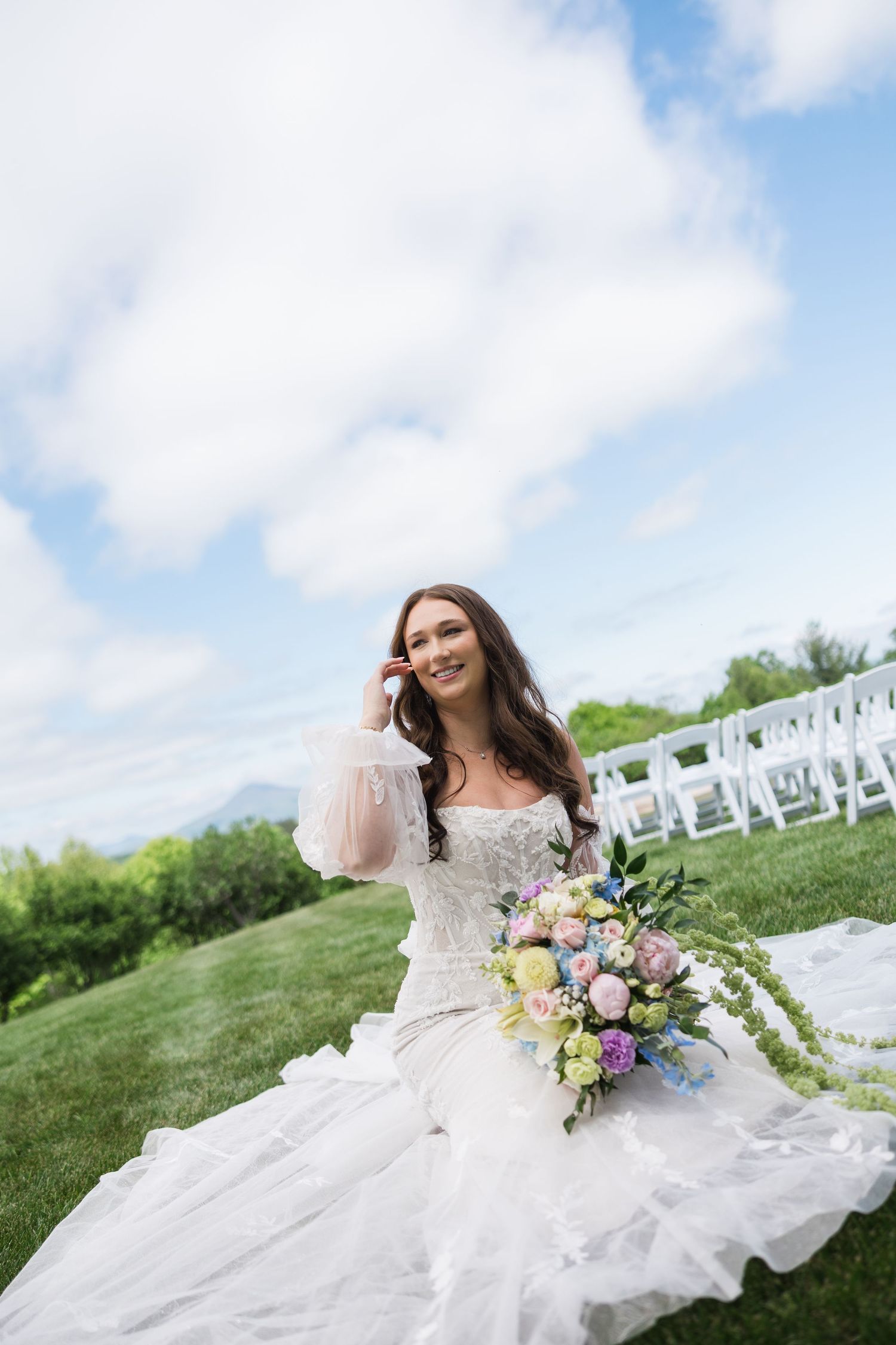 Smiling bride in lace gown holding colorful bouquet on green lawn.
