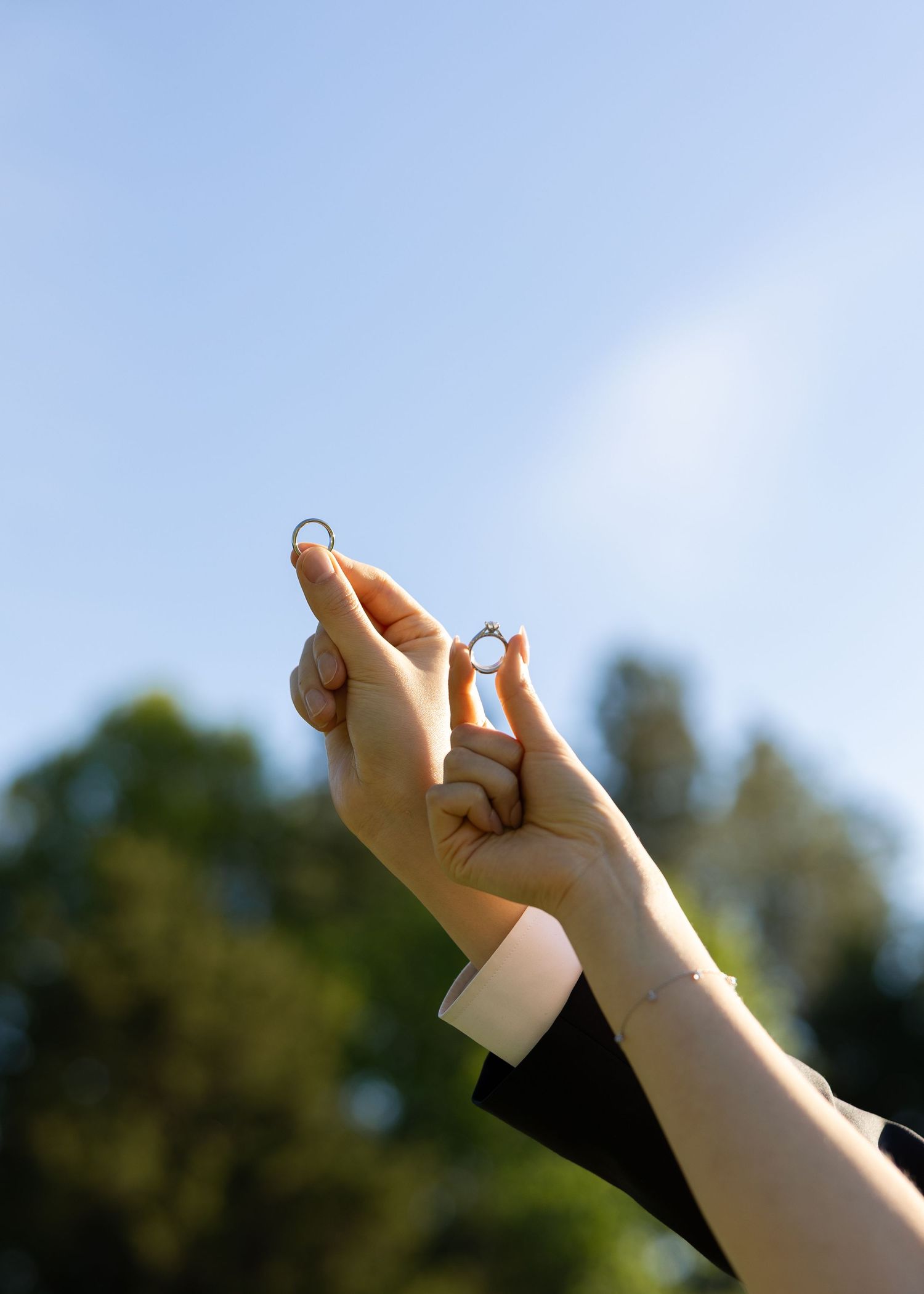 Two hands raised holding wedding rings against a bright blue sky.