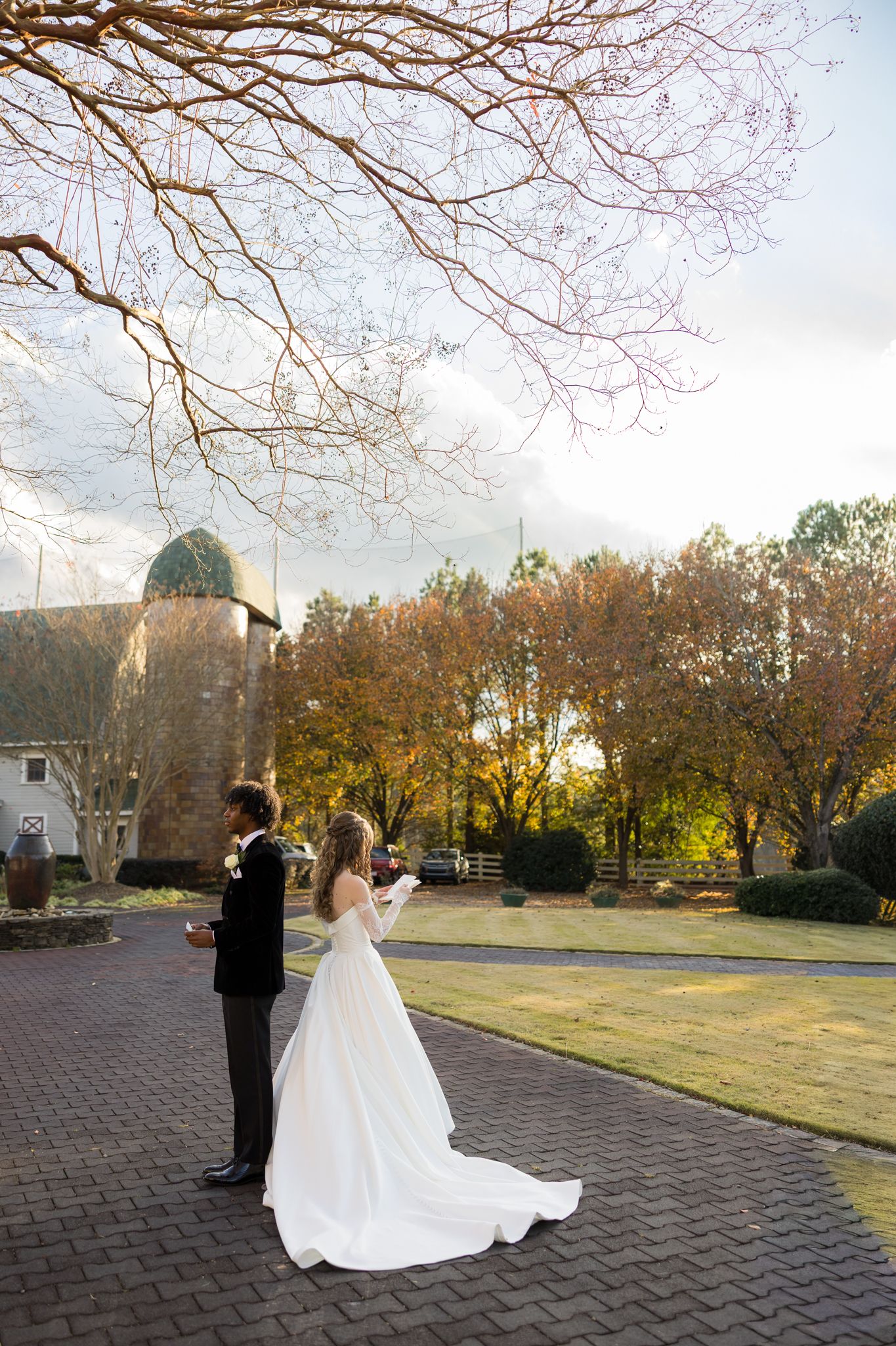 Bride and groom sharing first look moment on brick pathway surrounded by autumn trees at golden hour.