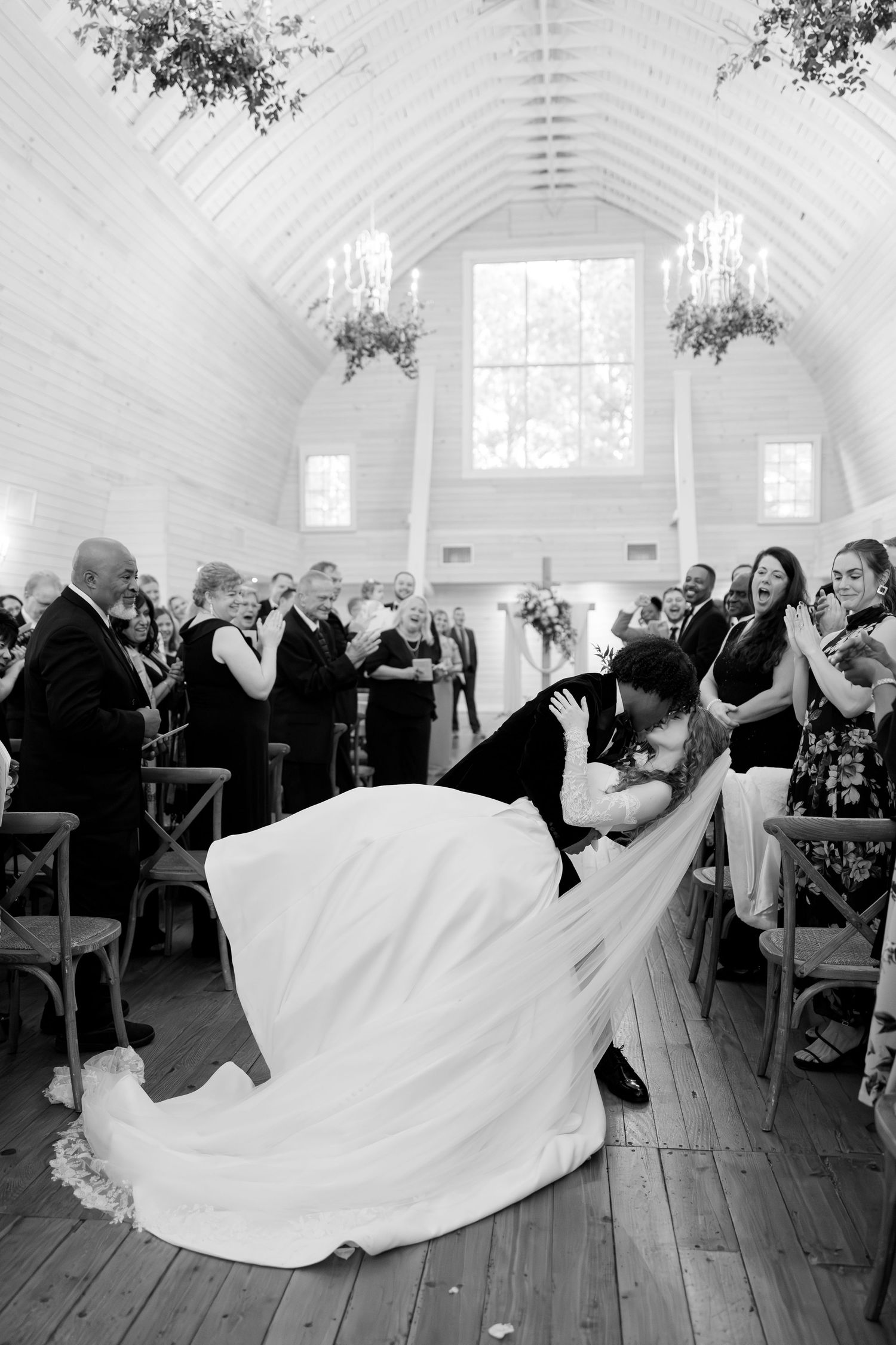 Black and white photo of groom dipping bride in a dramatic kiss at the wedding ceremony aisle.