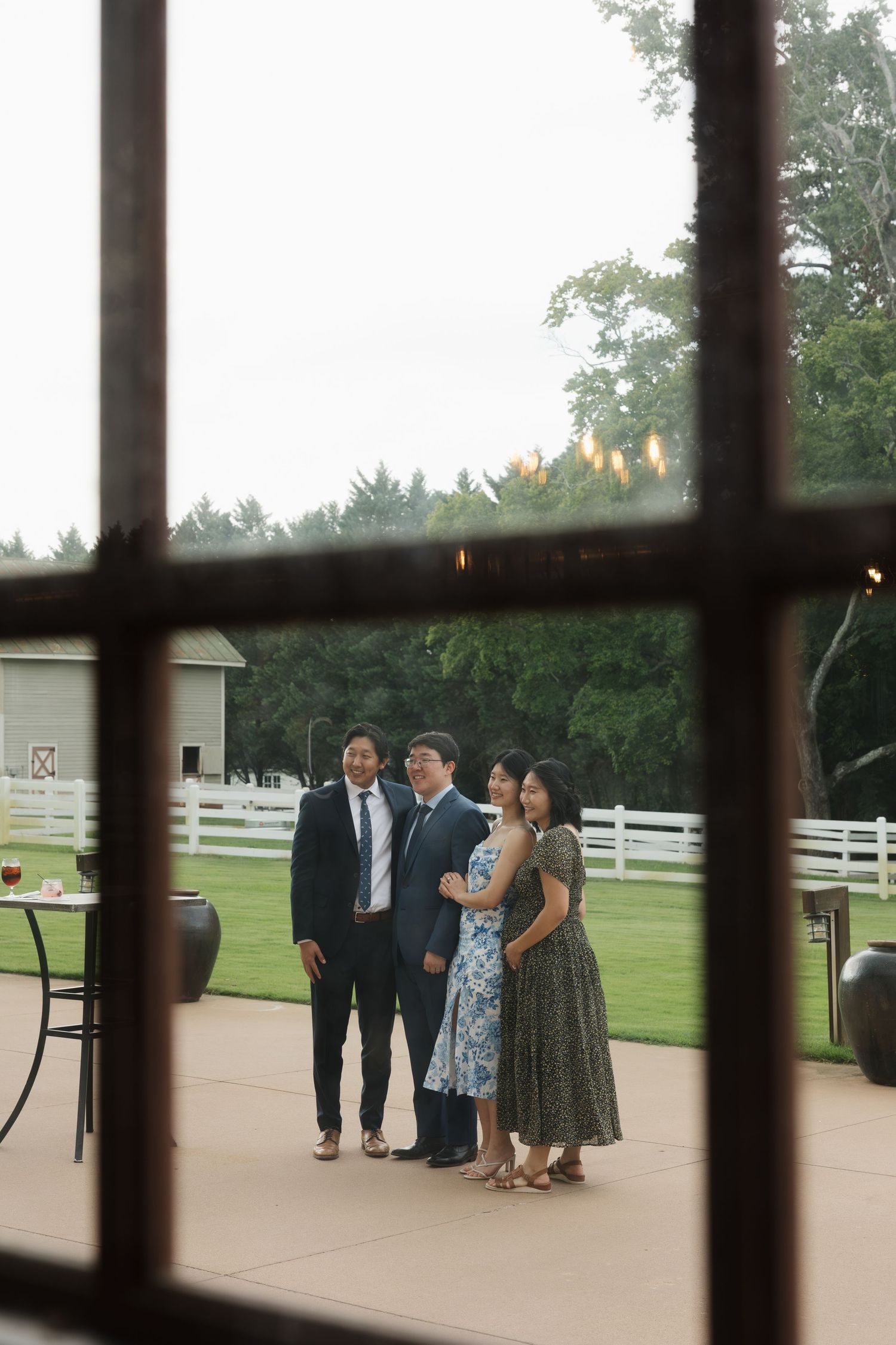 Four elegantly dressed guests pose together on a patio at a rustic farm wedding venue at dusk.