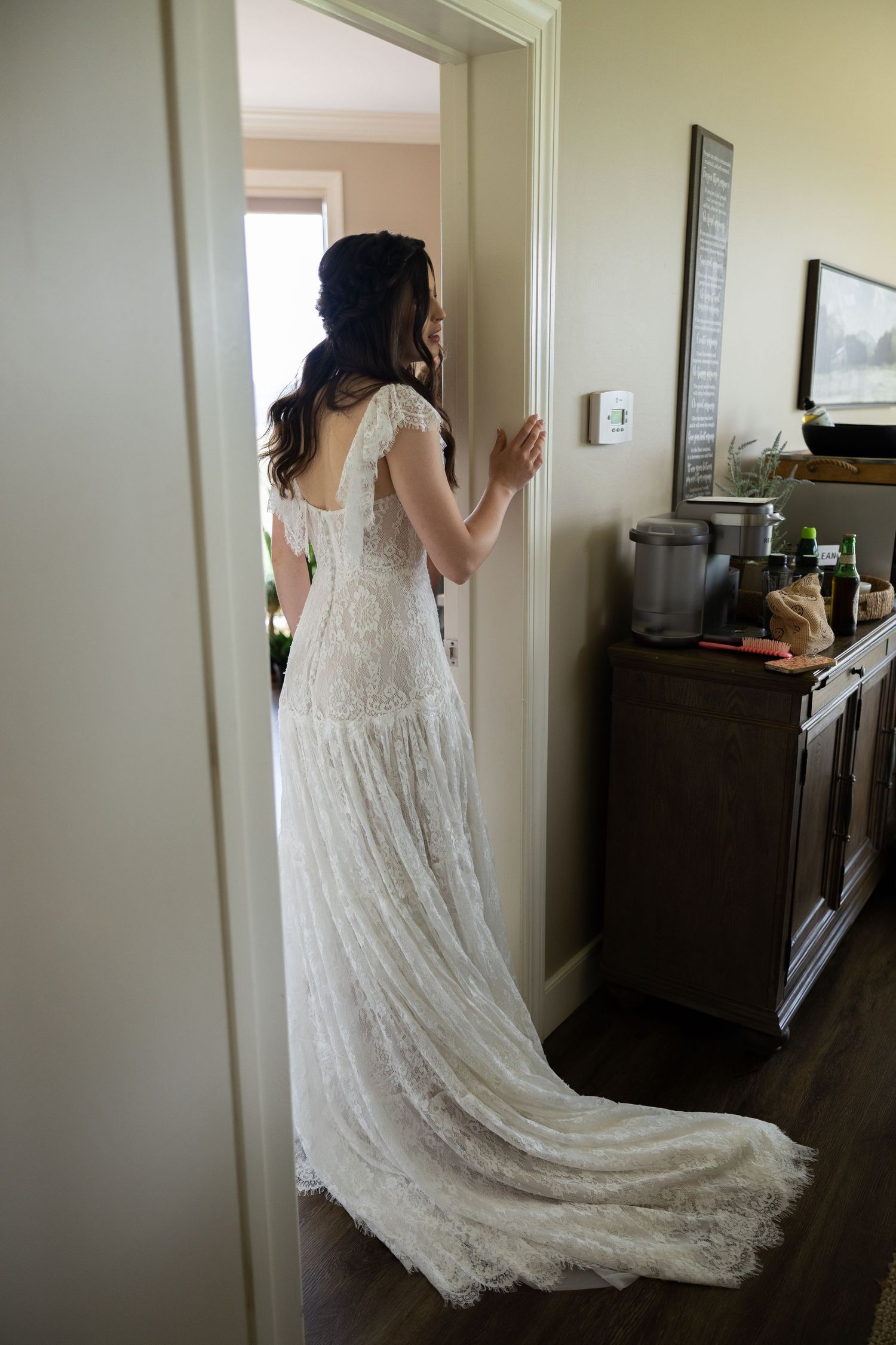 Bride in elegant lace wedding gown with train standing in a doorway viewed from behind.