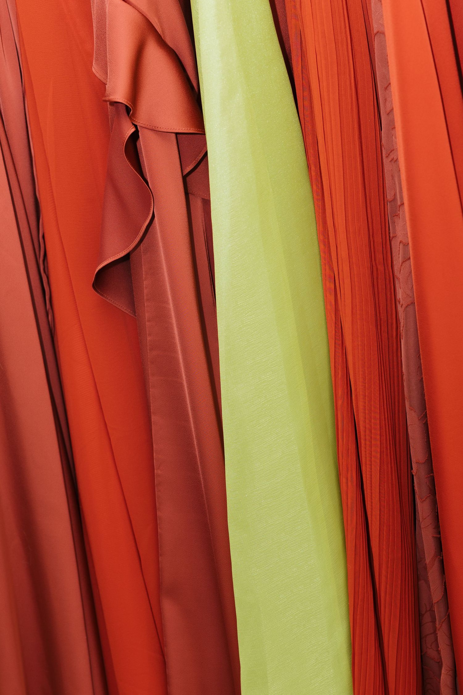 Vibrant red-orange and lime green flowing fabric panels hanging together, showcasing rich textile colors and draped folds.