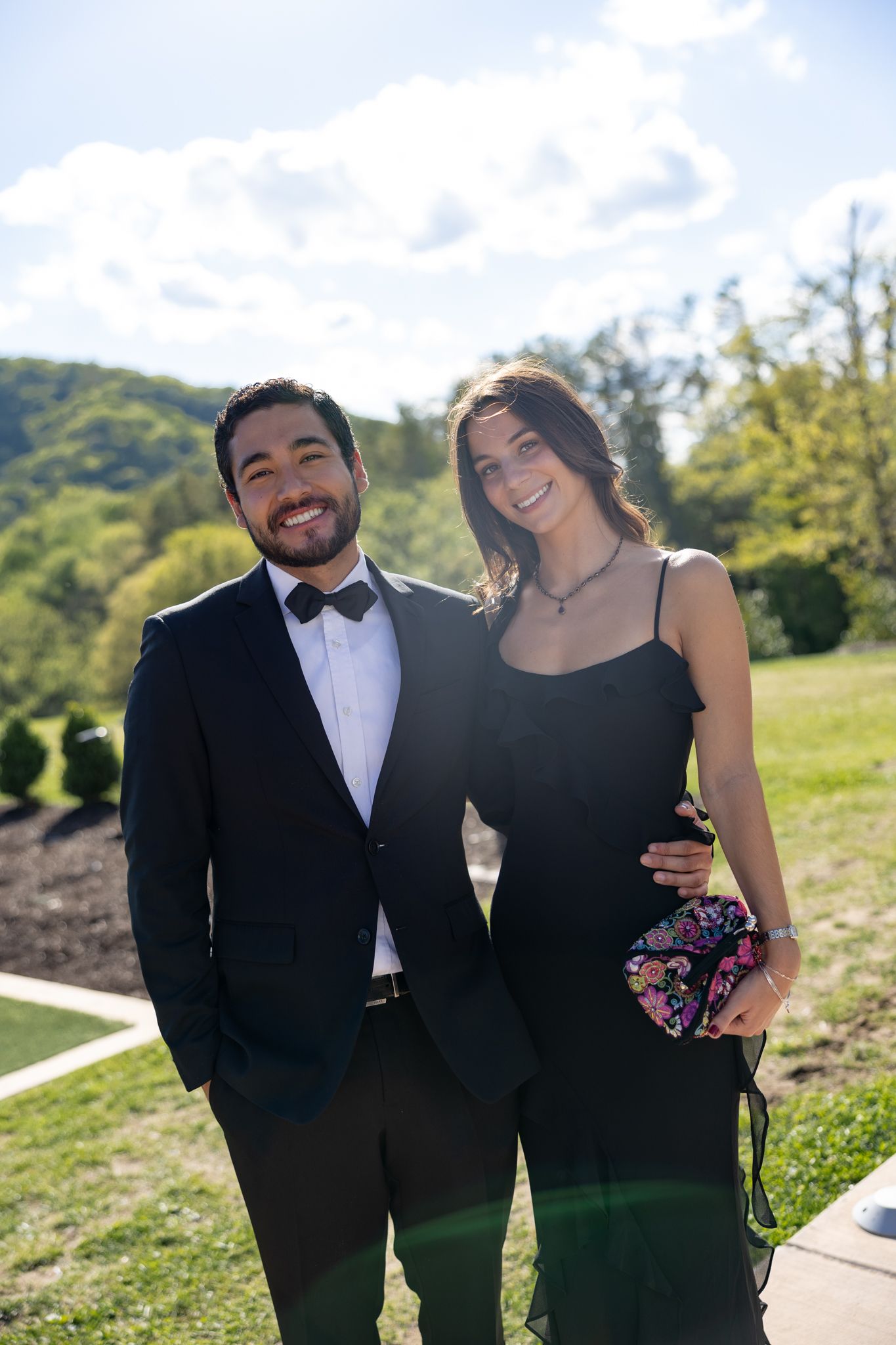 Smiling couple in black formal attire posing outdoors at a wedding celebration.