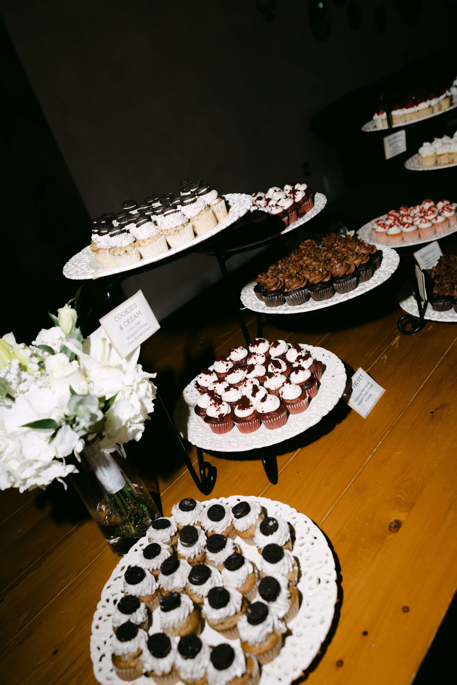 Elegant wedding dessert table featuring assorted cupcakes and mini treats displayed on tiered stands with white florals.