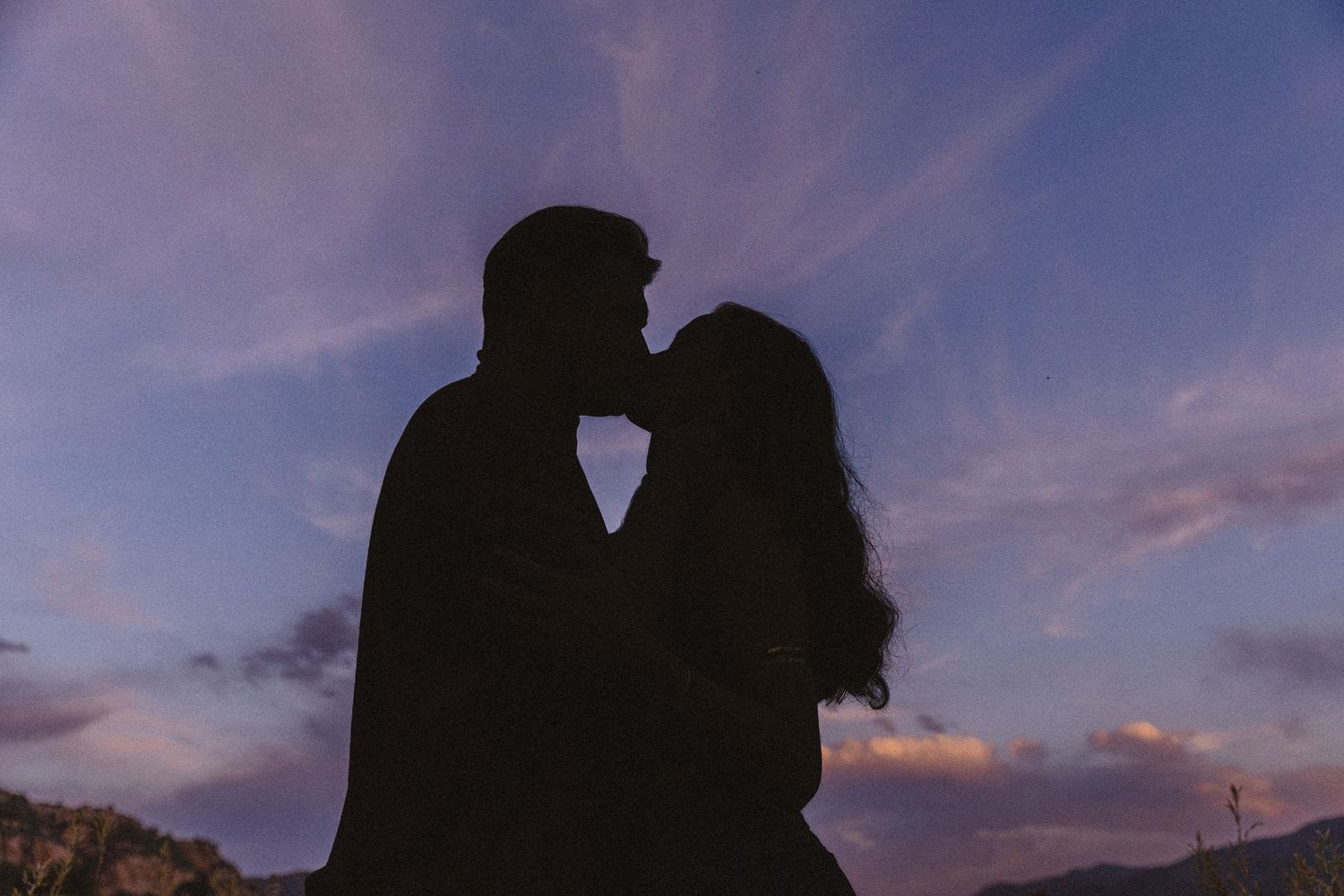 Silhouette of couple about to kiss against a vibrant purple and pink sunset sky.