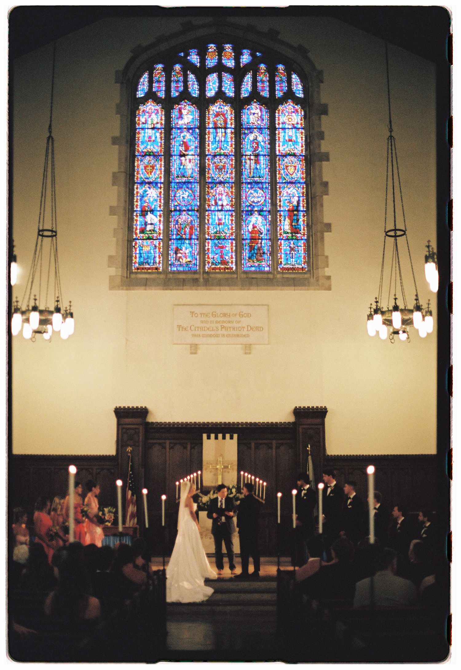 Elegant church wedding ceremony with stained glass window, candlelit altar, bride and groom exchanging vows before guests.