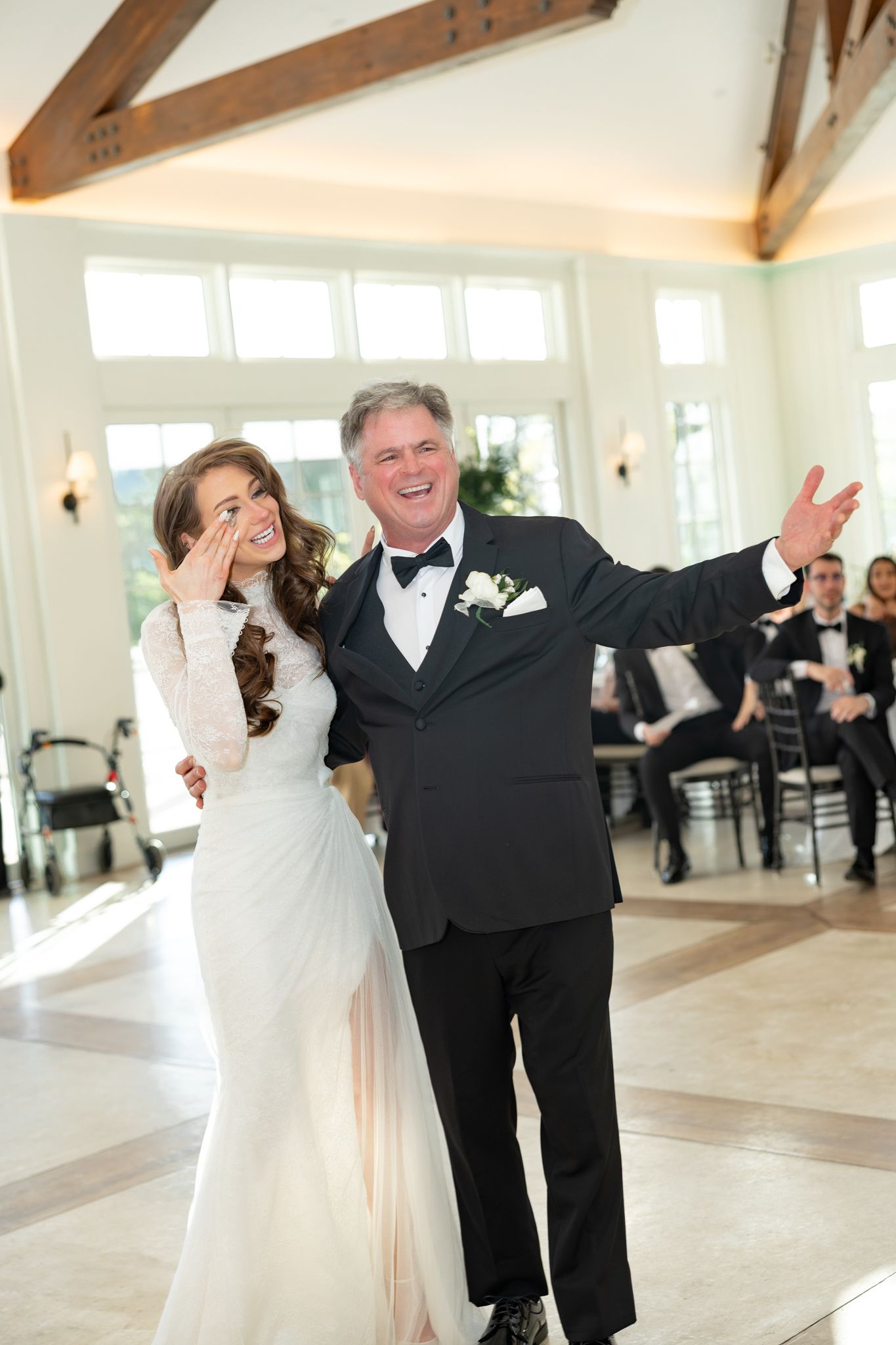 Bride and father share emotional first dance at elegant wedding reception in bright white venue.