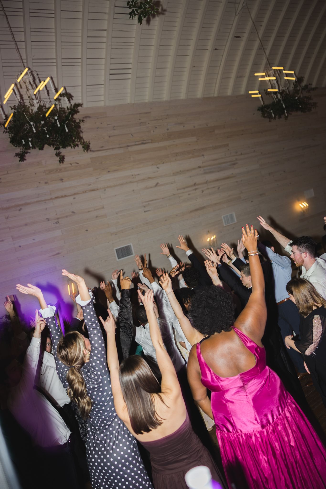 Wedding guests raise their hands on a packed dance floor during a lively reception celebration.