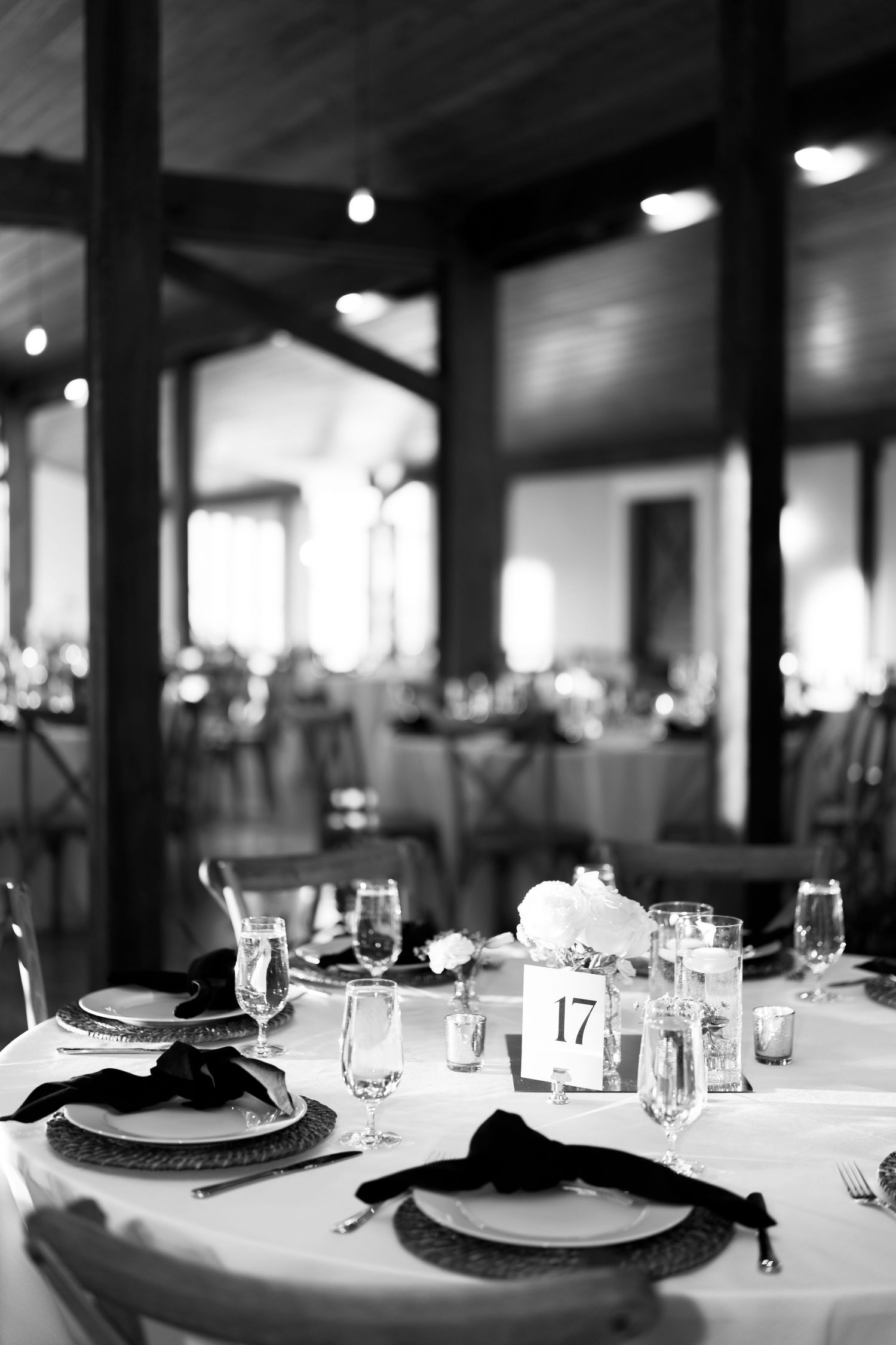 Black and white image of an elegant wedding reception table set with white florals, candles, and table number 17.