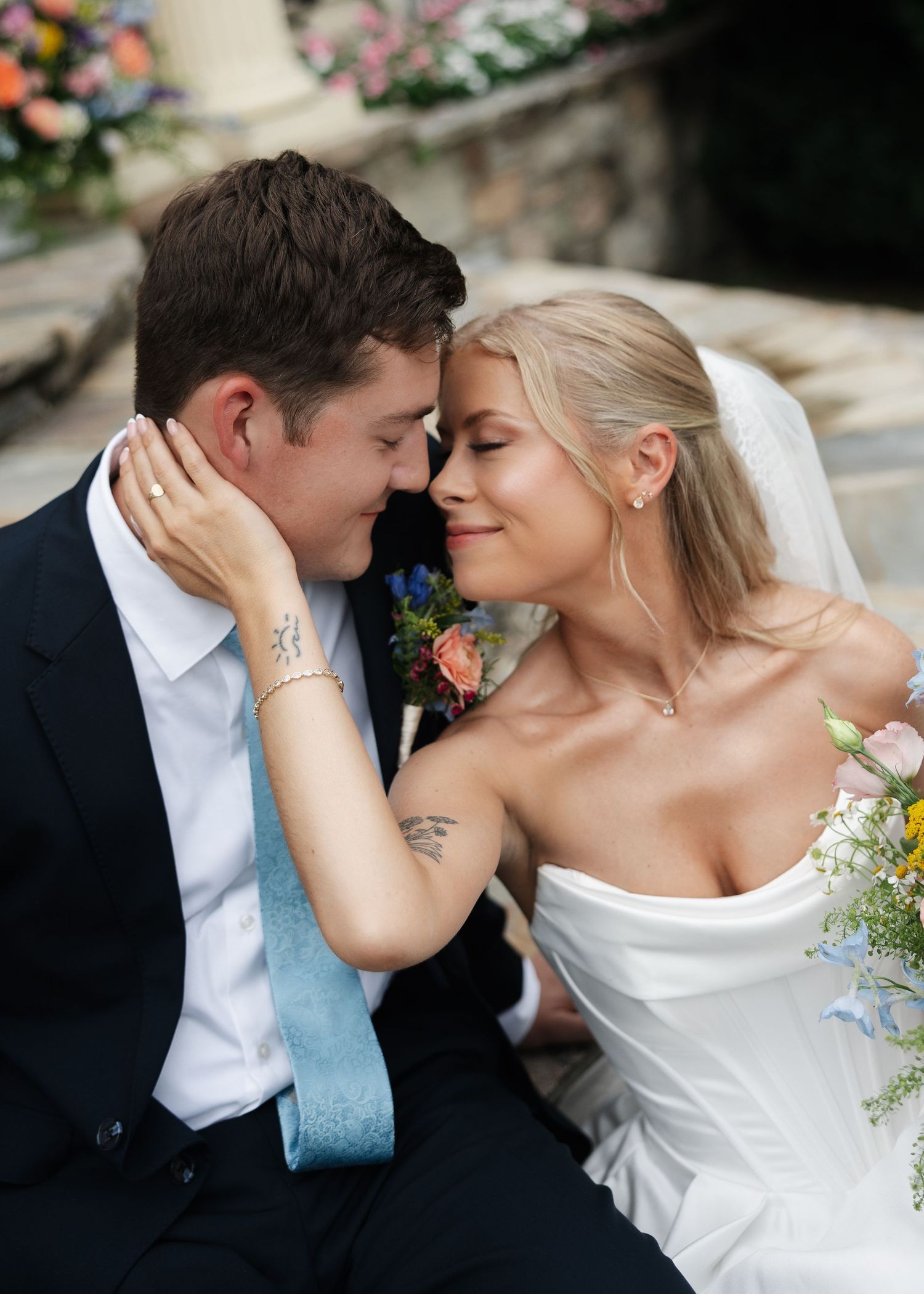 A bride and groom share an intimate moment, touching foreheads, as she holds a colorful bouquet on their wedding day.