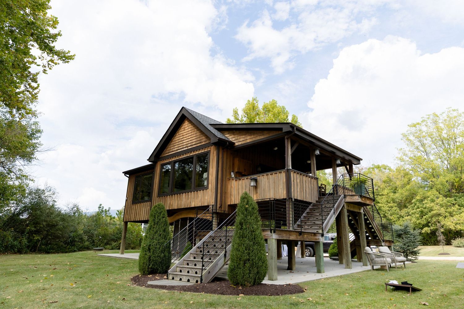 Rustic wooden wedding venue with wraparound deck and staircases surrounded by lush green trees and lawn.
